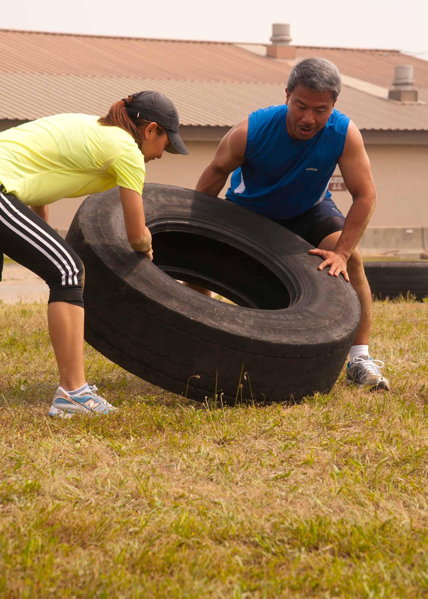 Chaplain (Capt.) Mario Rosario, 8th Fighter Wing, right, and Komang Goins, 8th Fighter Wing Airman ministry director, members of the Chapel team push their way through the fourth obstacle of the Wolf Pack Warrior Mud Run at Kunsan Air Base, Republic of Korea, June 8, 2013. Competitors were tasked to flip a tire from one end of the yard to the other as a team of two. (U.S. Air Force photo by Senior Airman Jessica Haas/ Released)