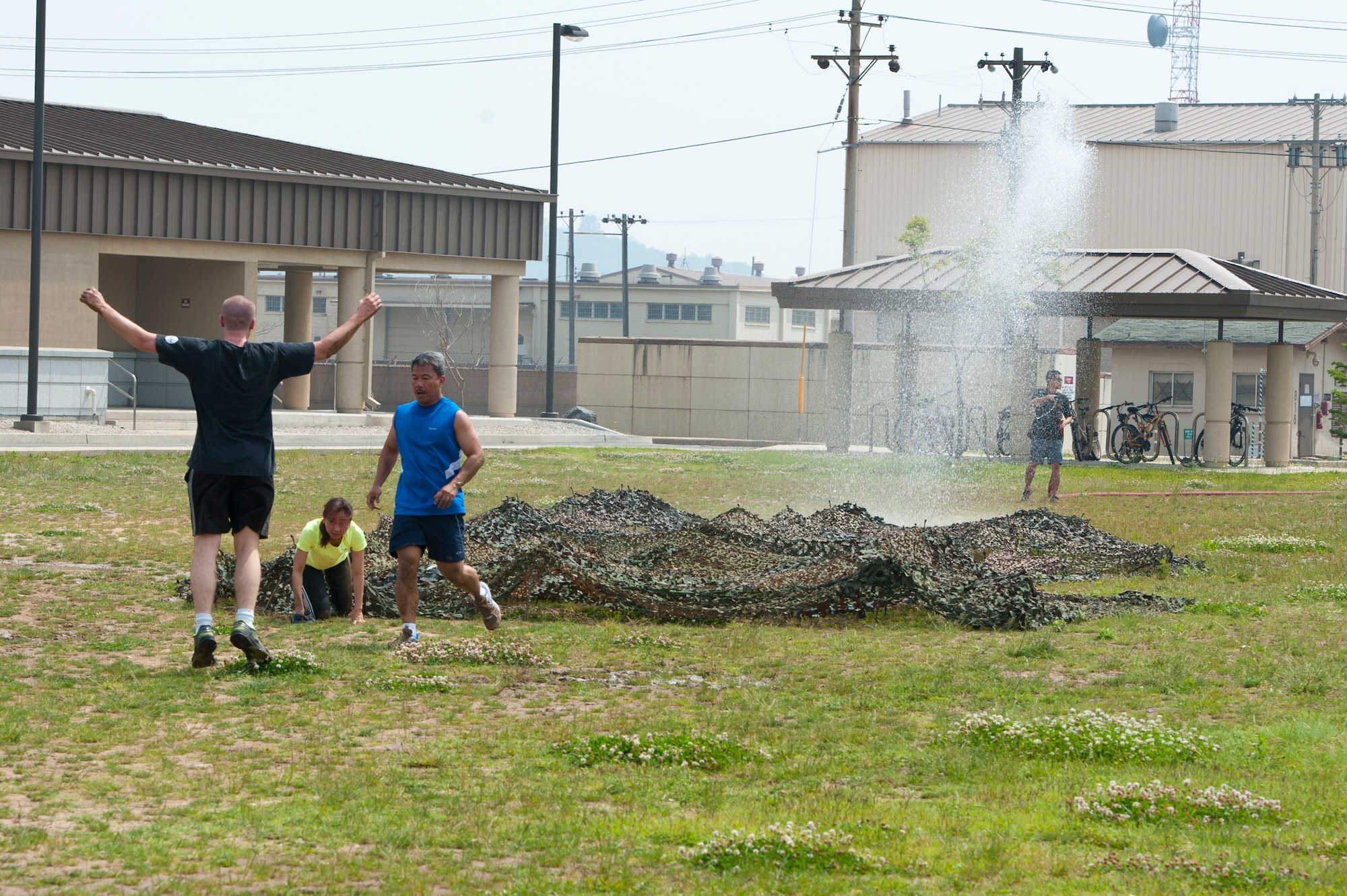 8th Fighter Wing Chapel team completes an obstacle while being sprayed with water during the Wolf Pack Warrior Mud Run at Kunsan Air Base, Republic of Korea, June 8, 2013. The obstacle required Airmen to low crawl through mud under camouflage netting. (U.S. Air Force photo by Staff Sgt. Jonathan Fowler/Released) 