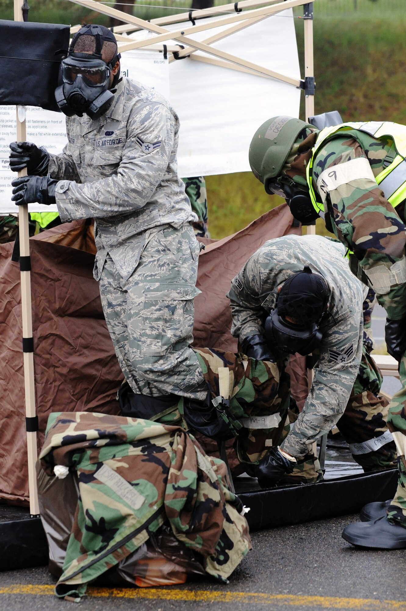 U.S. Air Force Airman 1st Class Cory Sumter, 35th Communications Squadron, has his protective over garment equipment removed by Senior Airman Reginald Washington, 35 CS, while passing through a contamination control area during an Operational Readiness Exercise at Misawa Air Base, Japan, June 18, 2013. CCA members watched over and advised pairs of Airmen as they performed proper decontamination procedures. (U.S. Air Force photo by Senior Airman Derek VanHorn)