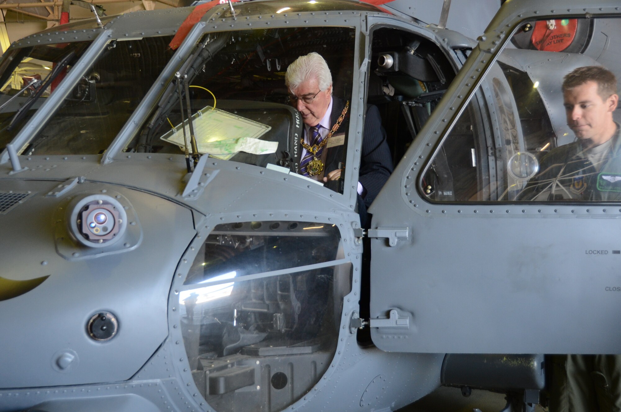 ROYAL AIR FORCE LAKENHEATH, England – Councillor Chris Barker (right), Forest Heath District Council chairman and Senior Airman Daniel Cowan (left), 56th Rescue Squadron special mission aviator, dicuss the basic functions of a HH-60G Pave Hawk helicopter during the summer orientation in Hangar 7 June 7, 2013. The guests witnessed a birds of prey demonstration, F-15C Eagle take-offs and landings, a military working dog demonstration, and static displays during their visit. (U.S. Air Force photo by Trevor T. McBride)