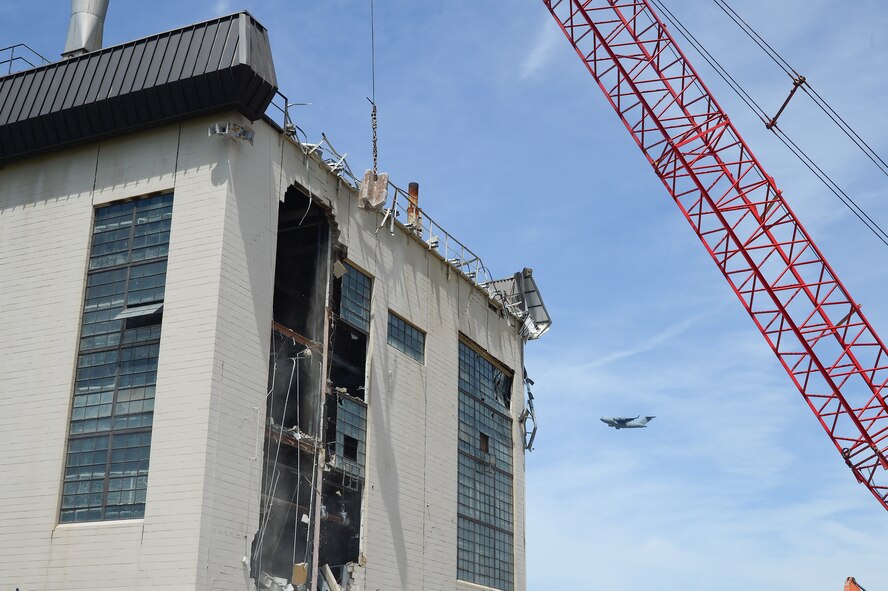 A 5-ton steel cutting ball swings toward the upper section of cinderblock wall during the demolition of Building 617 June 5, 2013, while a C-17A Globemaster III flies in the background at Dover Air Force Base, Del. The plant was replaced with a natural gas heating system that provides hot water and heat for the base. (U.S. Air Force photo/Greg L. Davis) 
