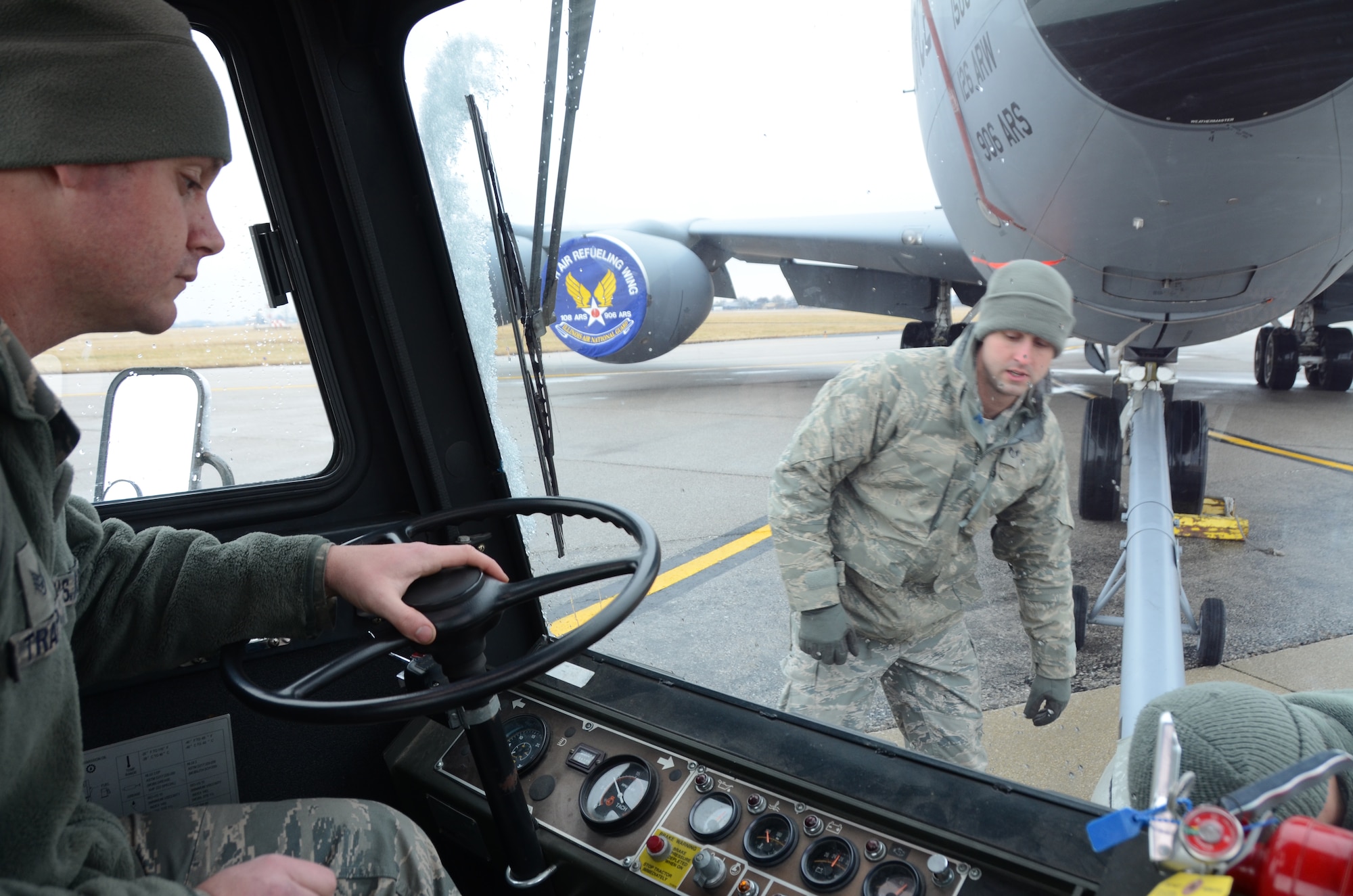 Staff Sgt. Mark Trapp (driver), a crew chief for the 906th Air Refueling Squadron, watches while Staff Sgt. Kenneth Baque (kneeling), a member of the 126th Maintenance Group, and Staff Sgt. David Polcyn, a member of the 906th Air Refueling Squadron, dismount the pivot point from the front of the aircraft tow vehicle while towing a KC-135R Stratotanker on Scott Air Force Base, Ill., March 5, 2013. The pivot point attaches to both the aircraft and the aircraft tow vehicle in order to ease movements. The 906 ARS is an Active  Associate squadron of the 126th Air Refueling Wing, Illinois Air National Guard, and is comprised of Active Duty Air Force members. (National Guard photo by Airman 1st Class Elise Stout)