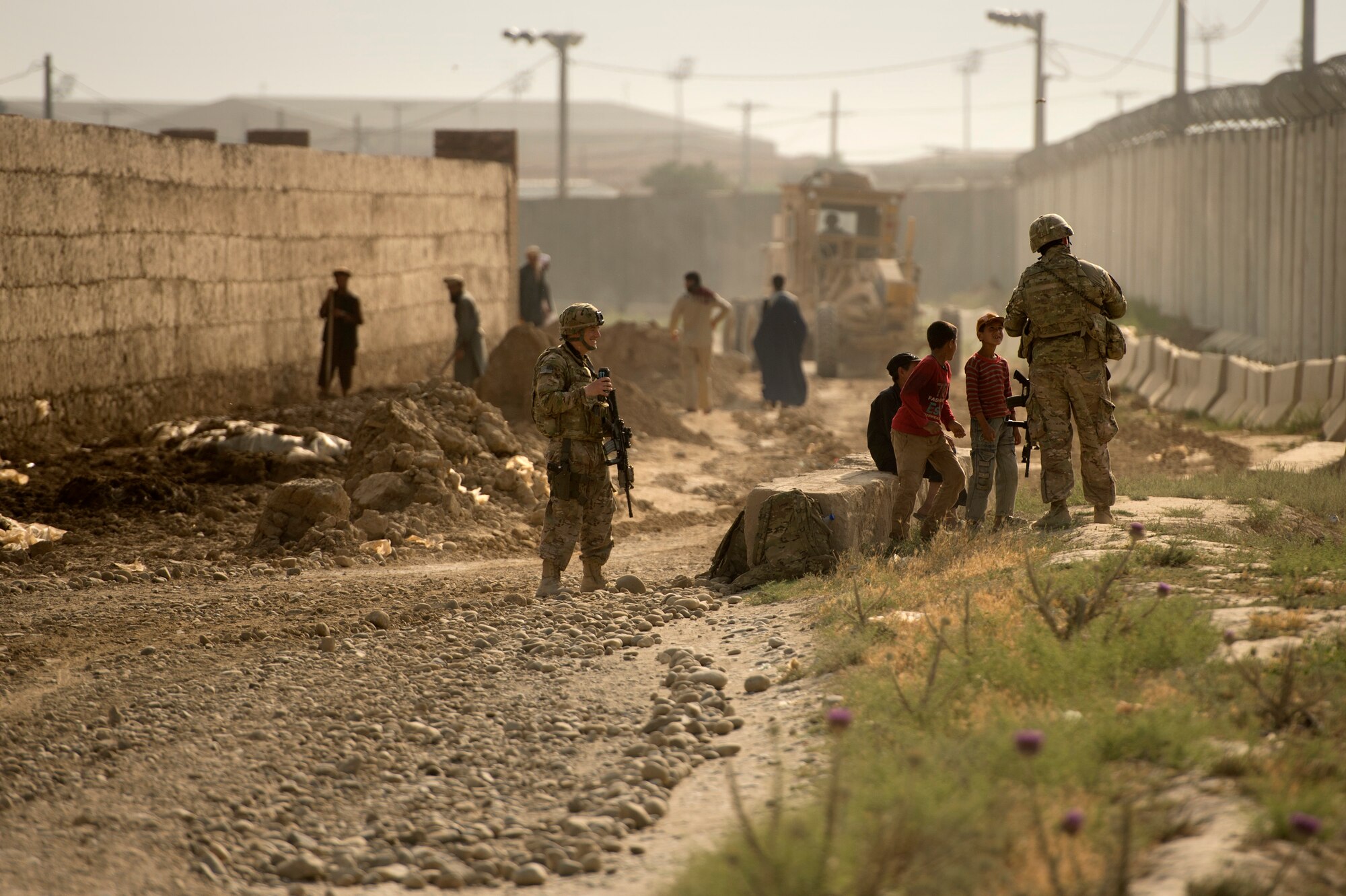 Tech. Sgts. Michael Bittner and Gemenie Strehlow, 455th Expeditionary Security Forces Group, talk with local Afghan youth during a security detail in the town of Payan Janqadam near Bagram Air Field, Afghanistan, June 13, 2013. Security forces airmen teamed up with 577th Expeditionary Prime Base Engineer Emergency Force Squadron pavement and heavy equipment “Dirt Boys” to rebuild a road connecting Payan Janqadam with Saka. Bittner hails from Fargo, N.D., and Strehlow from Grand Forks, N.D. Both are deployed from North Dakota Air National Guard. (USAF Photo/Master Sgt. Ben Bloker)
