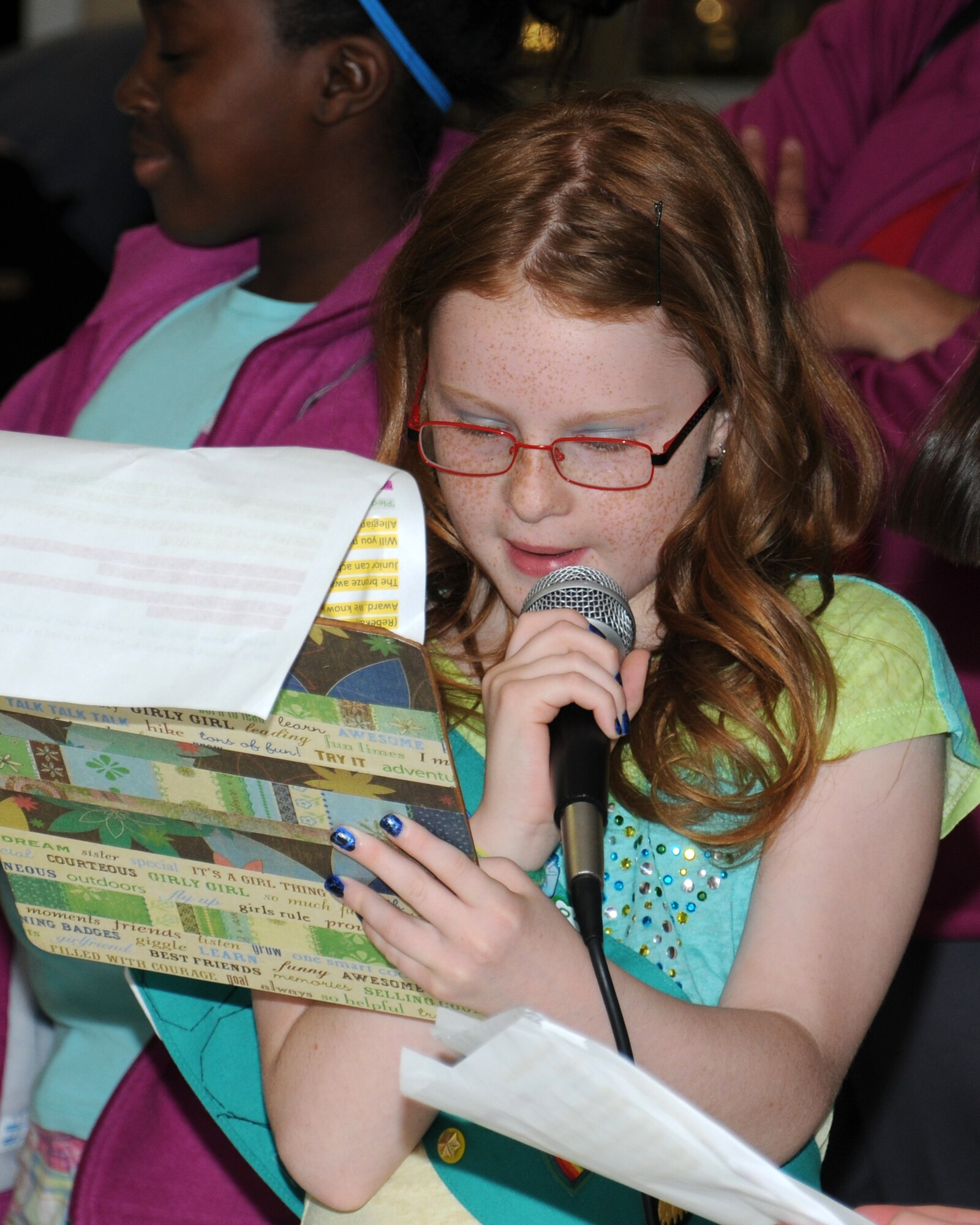 Olivia Tullis, 9, daughter of Master Sgt. Kent Tullis, 48th Aerospace Medicine Squadron NCO in charge of flight medicine at RAF Mildenhall and RAF Lakenheath, narrates during a charity fashion show June 14, 2013, at RAF Lakenheath, England. Junior Girl Scouts are girls who are in fourth or fifth grade. The girls chose to plan and host a fashion show in order to collect clothing donations for several local charities as well as for the Majengo Children's Home in Tanzania. (U.S. Air Force photo by Gina Randall/Released)