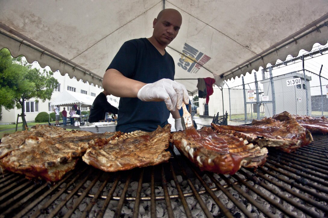 Gunnery Sgt. Ivan Davila, Headquarters and Headquarters Squadron Family Readiness Block Party volunteer, prepares ribs for the event, which took place behind barracks 313 and 314, June 15, 2013. Even with rain pouring throughout the entire event, Marines and sailors came out to enjoy the effort put forth by volunteers.
