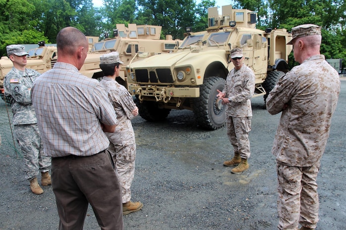 Lt. Col. Michael Burks (second from right), Joint Light Tactical Vehicle military deputy, stands in the "gap" between Mine Resistant Ambush Protected vehicles and a High Mobility Multipurpose Wheeled Vehicle (not shown in photo). He explains to Army and Marine Corps leadership that the JLTV will fill the capability "gap" that exists today in both services' light tactical vehicle fleets. This brief took place June 11 during the JLTV demonstration at the Transportation Demonstration Support Area on Marine Corps Base Quantico.