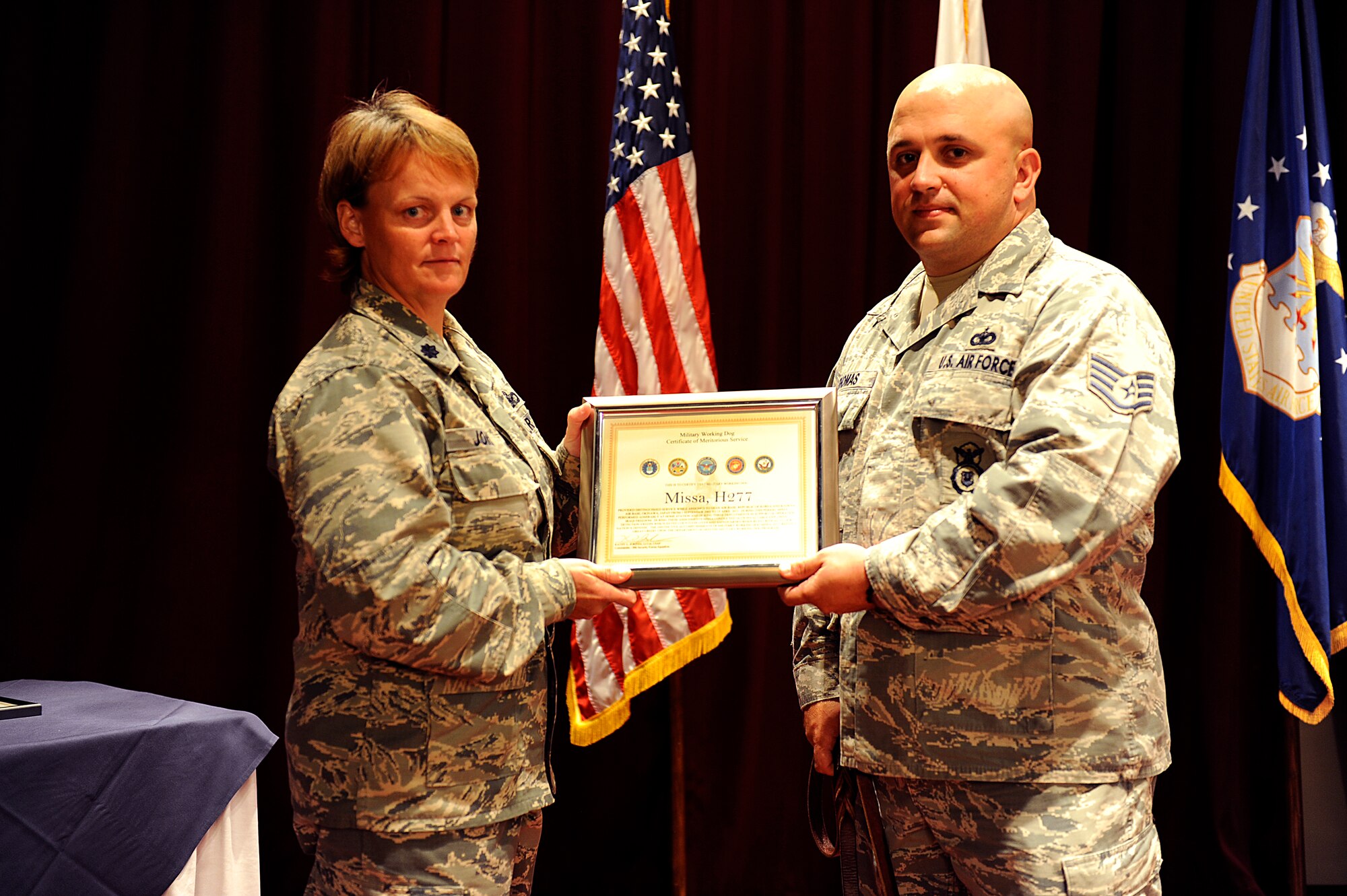 U.S. Air Force Lt. Col. Kathy Jordan, 18th Security Forces Squadron commander, presents Staff Sgt. Patrick Thomas, 18th Security Forces Squadron military working dog handler, and his newly adopted MWD, Missa, a MWD Certificate of Meritorious Service during the MWD retirement ceremony on Kadena Air Base, Japan, June 13, 2013. The four retiring MWDs, Missa, Shara, Nemo and Zina, performed nearly 60,000 detector sweeps collectively throughout their Air Force services. (U.S. Air Force photo by Senior Airman Maeson L. Elleman/Released)