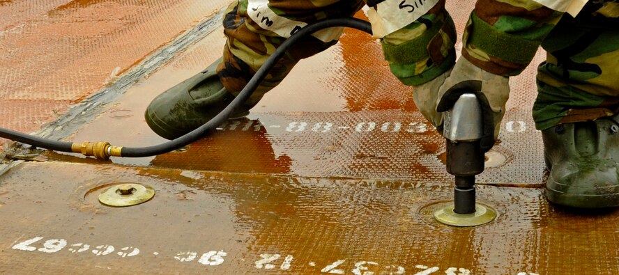 A U.S. Air Force Airman from 35th Civil Engineer Squadron drills bushings and anchors to a fiberglass mat after a simulated missile damaged the airfield during an Operational Readiness Exercise at Misawa Air Base, Japan, June 19, 2013. The 35 CES airfield damage control flight was tasked to rapidly repair the airfield and return it to an operational condition. (U.S. Air Force photo by Airman 1st Class Kenna Jackson)