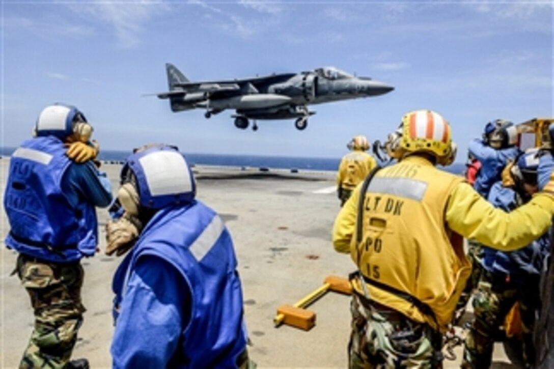 Flight deck crewmembers shield their faces from jet blast as an AV-8B Harrier lands on the amphibious assault ship USS Bonhomme Richard (LHD 6) during flight operations in the East China Sea on June 19, 2013.  The Bonhomme Richard Amphibious Ready Group is conducting joint force operations in the U.S. 7th Fleet area of responsibility.  The Harrier is assigned to Marine Attack Squadron 513.  