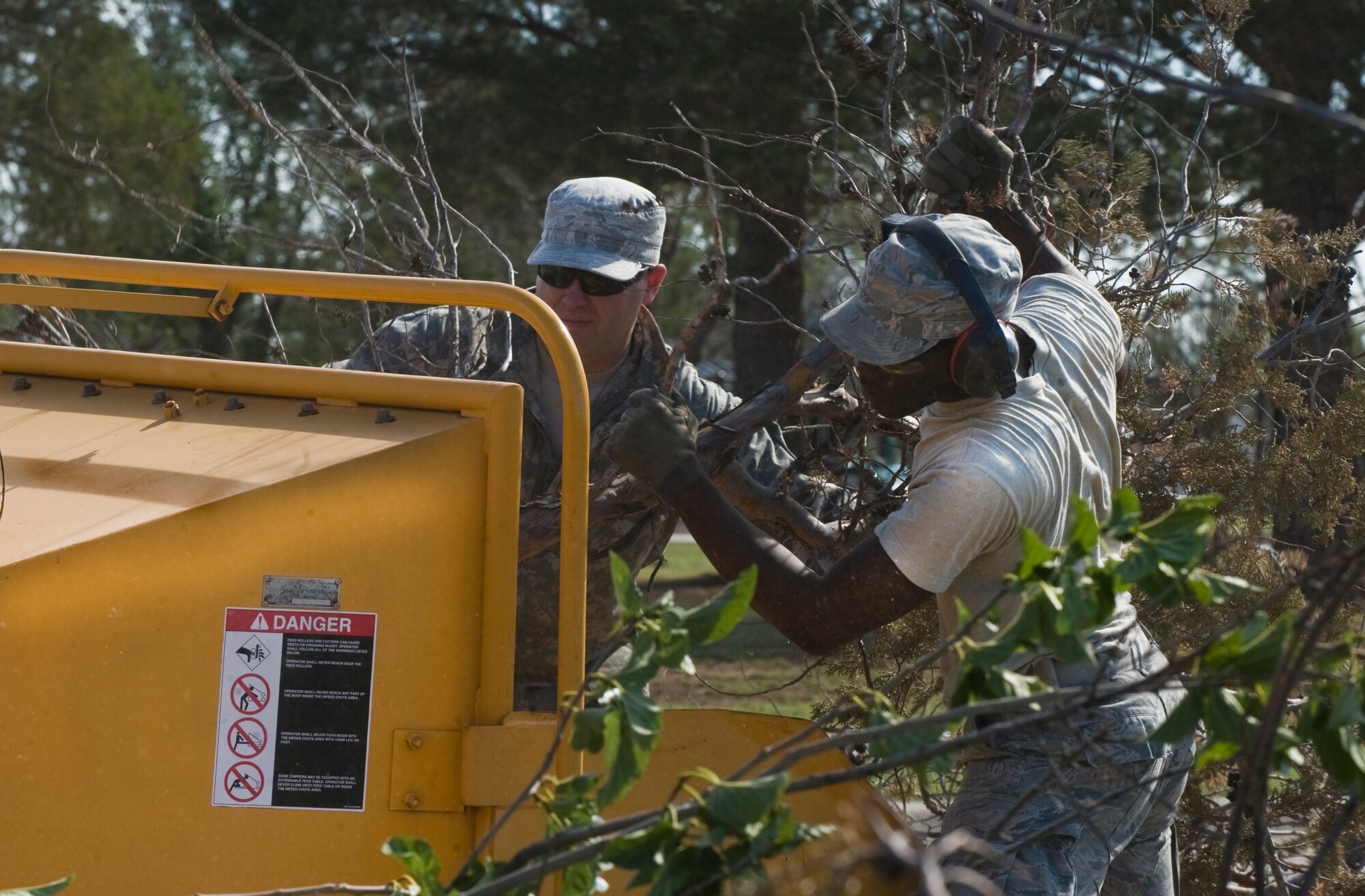 U.S. Air Force Staff Sgt. Jerry Ferguson, left, and Airman 1st Class Avery Shaw, right, from the 7th Civil Engineer Squadron (CES), push tree debris through a wood chipper June 18, 2013, at Dyess Air Force Base, Texas. After a storm that hit on June 17, subsided, Airmen from the 7th CES worked early in the morning to restore power to the base and clear roads of debris to ensure Dyess was mission ready. (U.S. Air Force photo by Senior Airman Jonathan Stefanko/Released)