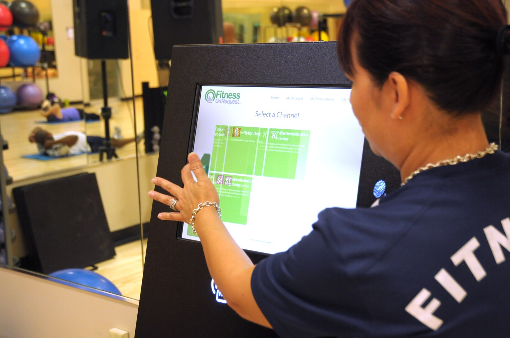 Kim Rennert, 902nd Force Support Squadron Fitness Assessment Cell evaluator, navigates the on-screen menu to select a workout for the Fitness On Request kiosk in Rambler Fitness Center at Joint Base San Antonio-Randolph June 12. The kiosk hosts a variety of programs, from kickboxing to Latin dance, all of which are currently set for 35 minutes. (U.S. Air Force photo by Alexandria Slade/ Released)