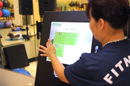 Kim Rennert, 902nd Force Support Squadron Fitness Assessment Cell evaluator, navigates the on-screen menu to select a workout for the Fitness On Request kiosk in Rambler Fitness Center at Joint Base San Antonio-Randolph June 12. The kiosk hosts a variety of programs, from kickboxing to Latin dance, all of which are currently set for 35 minutes. (U.S. Air Force photo by Alexandria Slade/ Released)