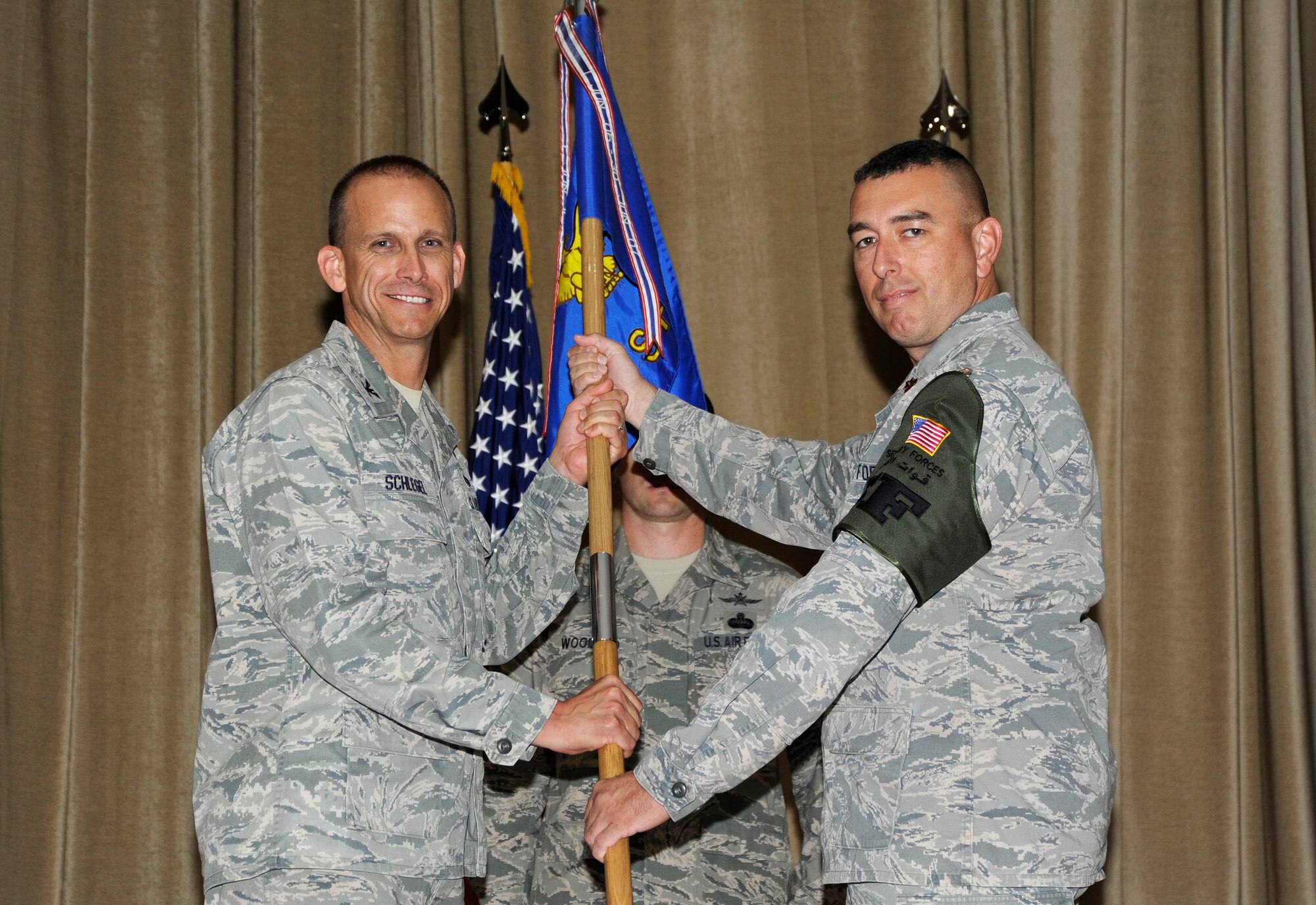 Colonel Charles F. Schlegel, 387th Air Expeditionary Group commander, left, passes the 387th Expeditionary Security Forces Squadron guidon to Maj. Thomas M. McGillicuddy during a change of command ceremony at an undisclosed location in Southwest Asia June 21, 2013. McGillicuddy assumed command of the 387th ESFS from Capt. Aaron W. Williams. (U.S. Air Force photo by Master Sgt. Christopher A. Campbell)