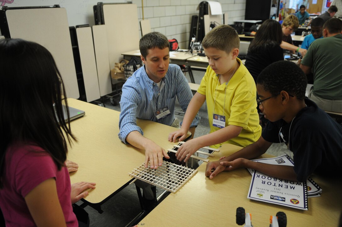 Louis Holko, a systems engineer at Marine Corps Systems Command, explains to rising seventh-grader Mackenzie and rising eighth-grader Emmanuel why one of their team’s balsa wood bridges is stronger than the other. With help from volunteers from MCSC and other organizations, participants in Quantico Middle/High School’s weeklong Science, Technology, Engineering and Math Academy built and tested the bridges on June 21, 2013.