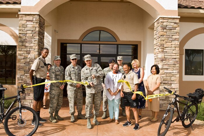 Col. Barry Cornish, 99th Air Base Wing commander, cuts a ribbon signifying the official opening of the new 99th Security Forces Squadron substation while military members and civilians watch during a ceremony at the base housing community center June 24, 2013, at Nellis Air Force Base, Nev. The substation and bike patrol will provide a less threatening and more visible security forces presence within the housing community. (U.S. Air Force photo by Airman 1st Class Christopher Tam)