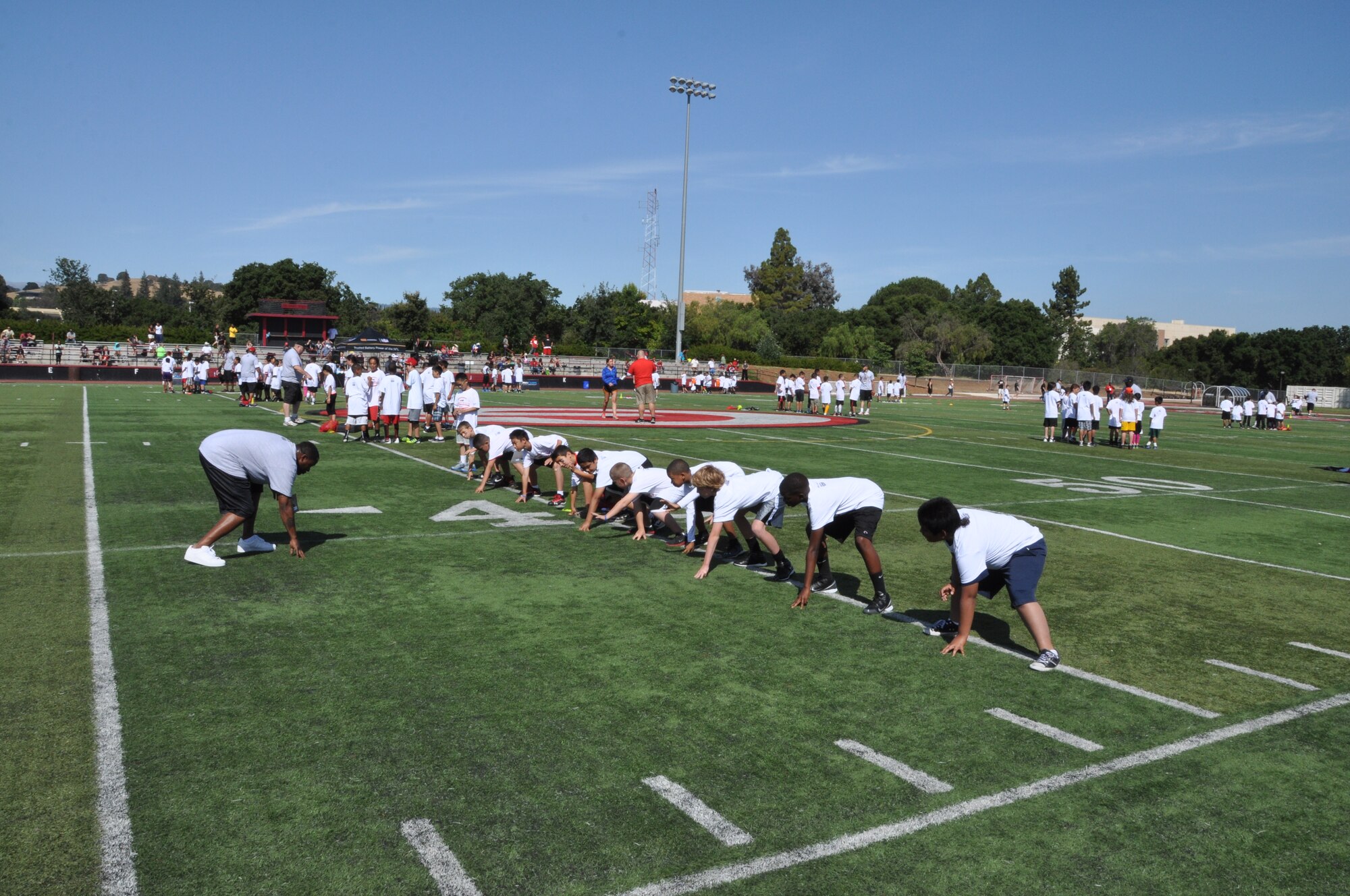 A group of children mimic their coach’s three-point stance. The three-point-stance is a fundamental skill for any lineman or halfback. (U.S. Air Force photo/Staff Sgt. Christopher Carranza)