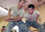 Army Pfc. Ji Chong, left, listens to an instructor while putting a submission hold on Army Pfc. Andrew Bituin during a nonlethal weapons training class at Muscatatuck Urban Training Center near Camp Atterbury, Ind. The training, designed to induce compliance and control rather than injury, is part of deployment training for Chong and Bituin's unit, 40th Infantry Division, which is scheduled to deploy to Kosovo.