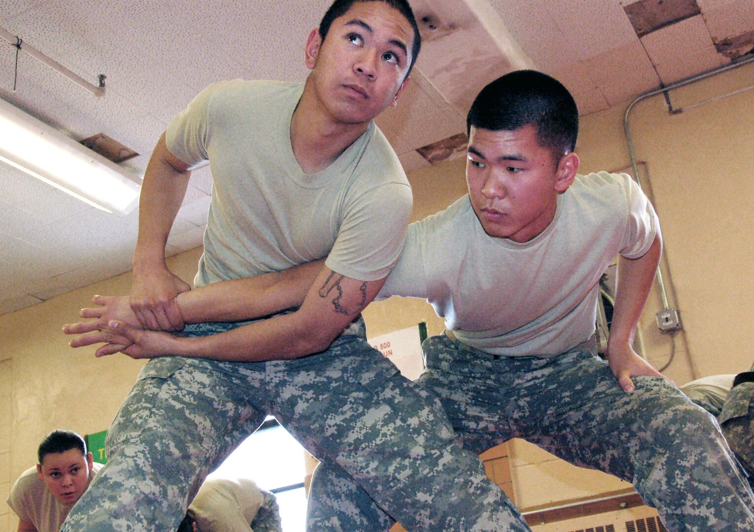 Army Pfc. Ji Chong, left, listens to an instructor while putting a submission hold on Army Pfc. Andrew Bituin during a nonlethal weapons training class at Muscatatuck Urban Training Center near Camp Atterbury, Ind. The training, designed to induce compliance and control rather than injury, is part of deployment training for Chong and Bituin's unit, 40th Infantry Division, which is scheduled to deploy to Kosovo.