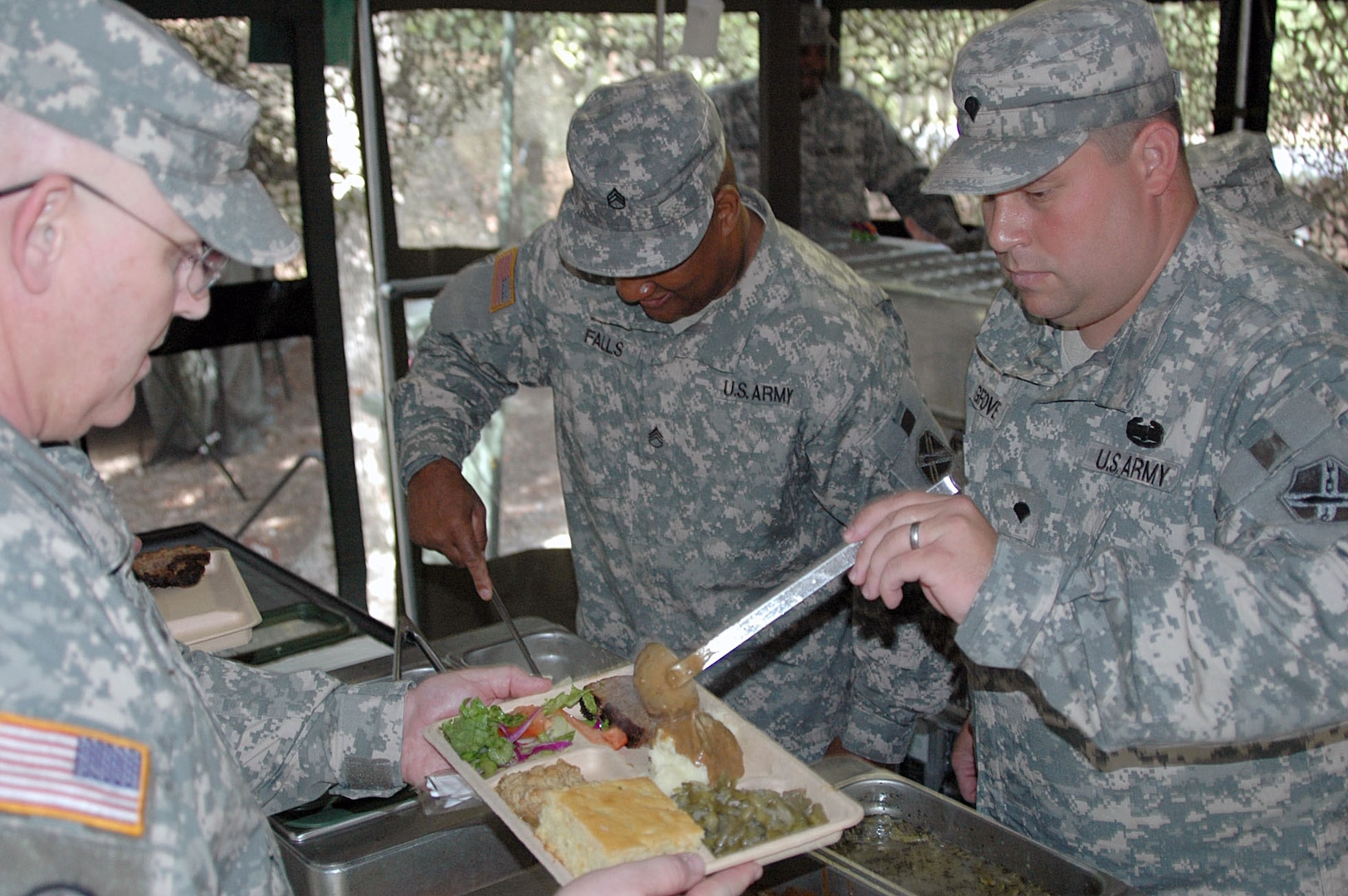 Army Staff Sgt. Joey K. Falls (left) and Spc. Seth Grove (right) of the Virginia National Guard's 1032nd Transportation Company serve 1st Sgt. Ernest T. Miller out of a mobile kitchen trailer. The mobile kitchen trailer was set up as a requirement of the Connelly Competition for which they were competing.