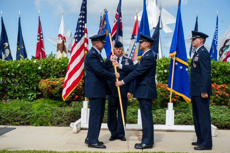 Col. Johnny Roscoe, 15th Wing commander (left) passes the 15th Operations Group guidon to incoming commander, Col. Michael Merritt, (middle) as former commander, Col. Dan Baldessari, (right) looks on during the 15 OG change of command ceremony at the Missing Man Formation on Joint Base Pearl Harbor-Hickam, Hawaii, June 21, 2013.  The change of command ceremony is a military tradition deeply rooted in history and dates back to the times of the Roman Legion. In that period, military organizations developed flags that were unique to the organization with specialized colors and designs. When soldiers followed their leaders into battle, they kept sight of the flag. If the banner still waved after the conflict, it was a sign that their side had won. Having this position of importance, the flag was incorporated into change of command ceremonies. The organizational banner was exchanged in public for all to see that the one who holds the flag is the unchallenged leader of the armies. The modern day ceremony is principally symbolic, yet it still indicates to all the authority of the incoming commander in the finest military traditions. (U.S. Air Force Photo/Staff Sgt. Terri Paden)