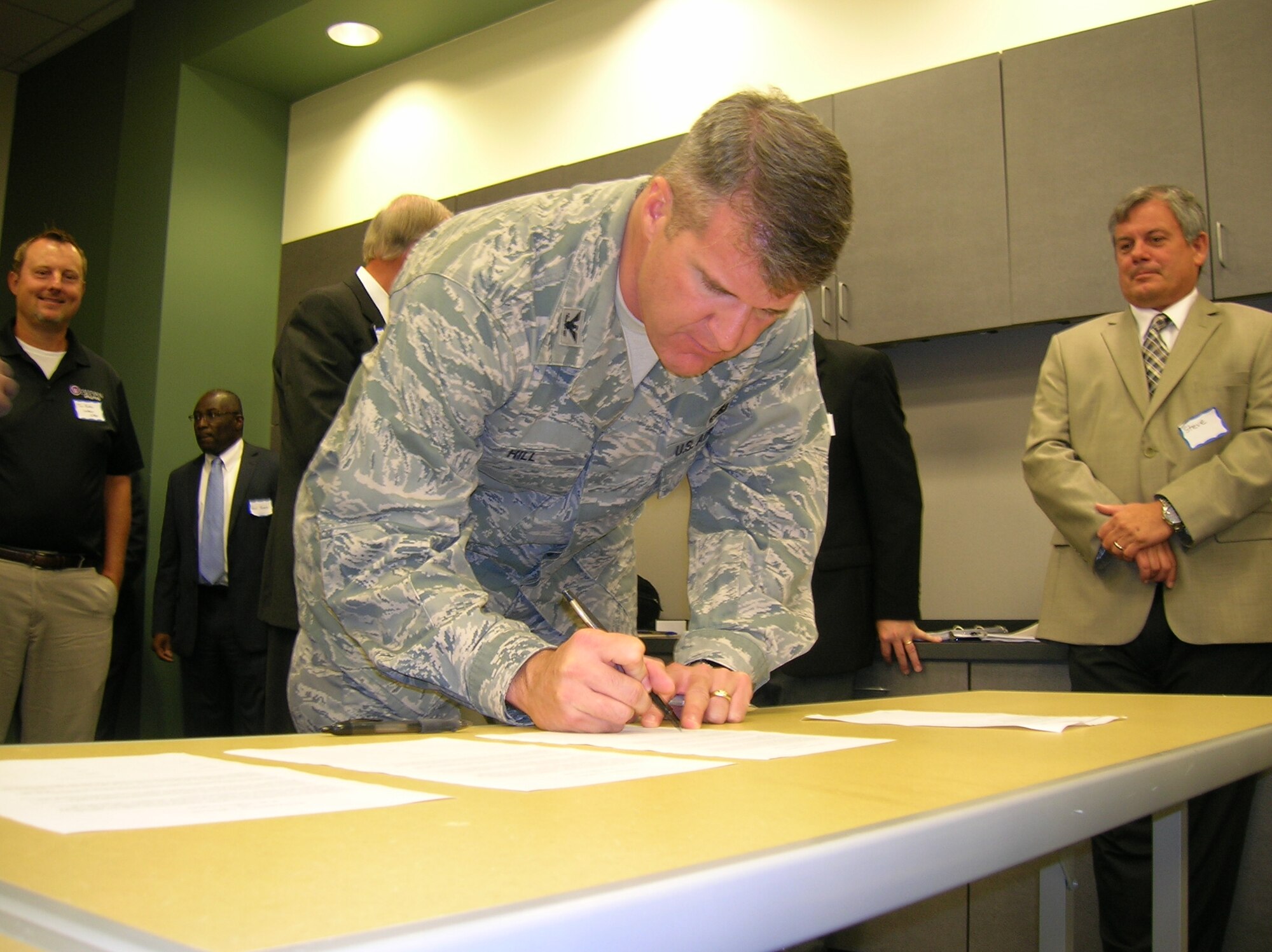 Col. Christopher Hill, Installation commander, signs one of four agreements June 24, 2013, as part of a new community partnership program. The program, called the Air Force Community Partnership Initiative, was created to explore cost-saving opportunities through partnerships and shared services with local communities and the private sector. (U.S. Air Force photo by Roland Leach)
