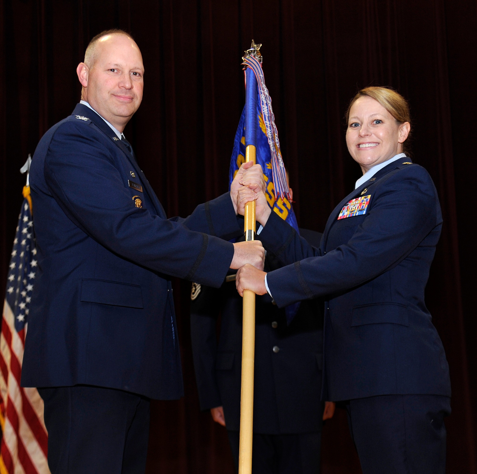 Col. Konrad Klausner, 92nd Mission Support Group commander, hands off the guidon to Maj. Maria Hatchett, 92nd Force Support Squadron commander, during the 92nd FSS change of command ceremony inside the base theather at Fairchild Air Force Base, Wash., June 21, 2013. The change of command ceremony is a tradition that represents a formal transfer of authority and responsibility. (U.S. Air Force photo by Airman 1st Class Ryan Zeski)