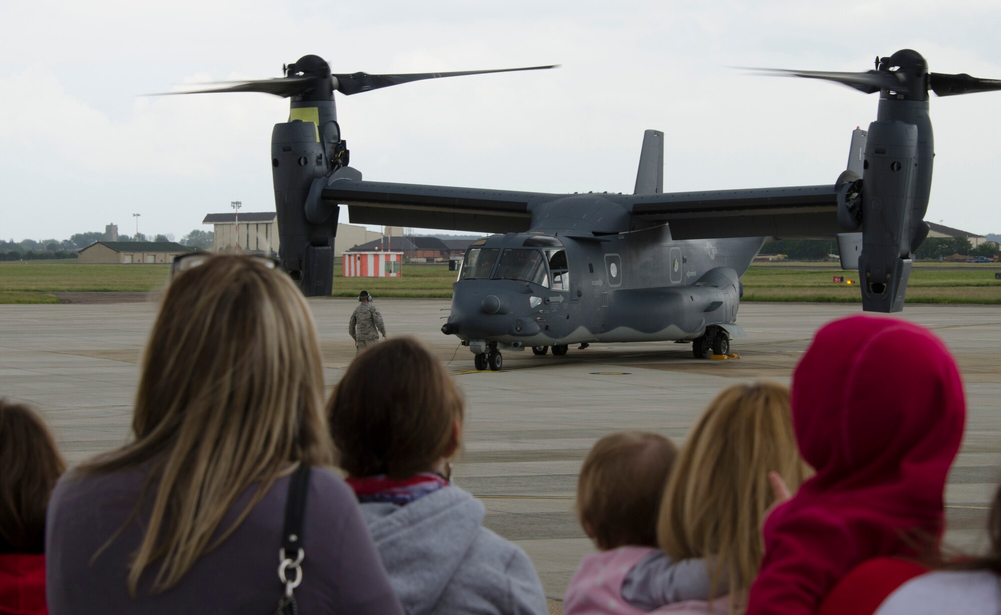 Team Mildenhall members look on as a CV-22B Osprey prepares to shut down June 24, 2013, on RAF Mildenhall, England. The CV-22 fills part of the role previously accomplished by the MH-53 Pave Low helicopter at the 352nd Special Operations Group. However, the Osprey combines the vertical takeoff, hover and vertical-landing qualities of a helicopter with the long-range, fuel-efficiency and speed of a turboprop aircraft. (U.S. Air Force photo by Staff Sgt. Stephen Linch/Released)