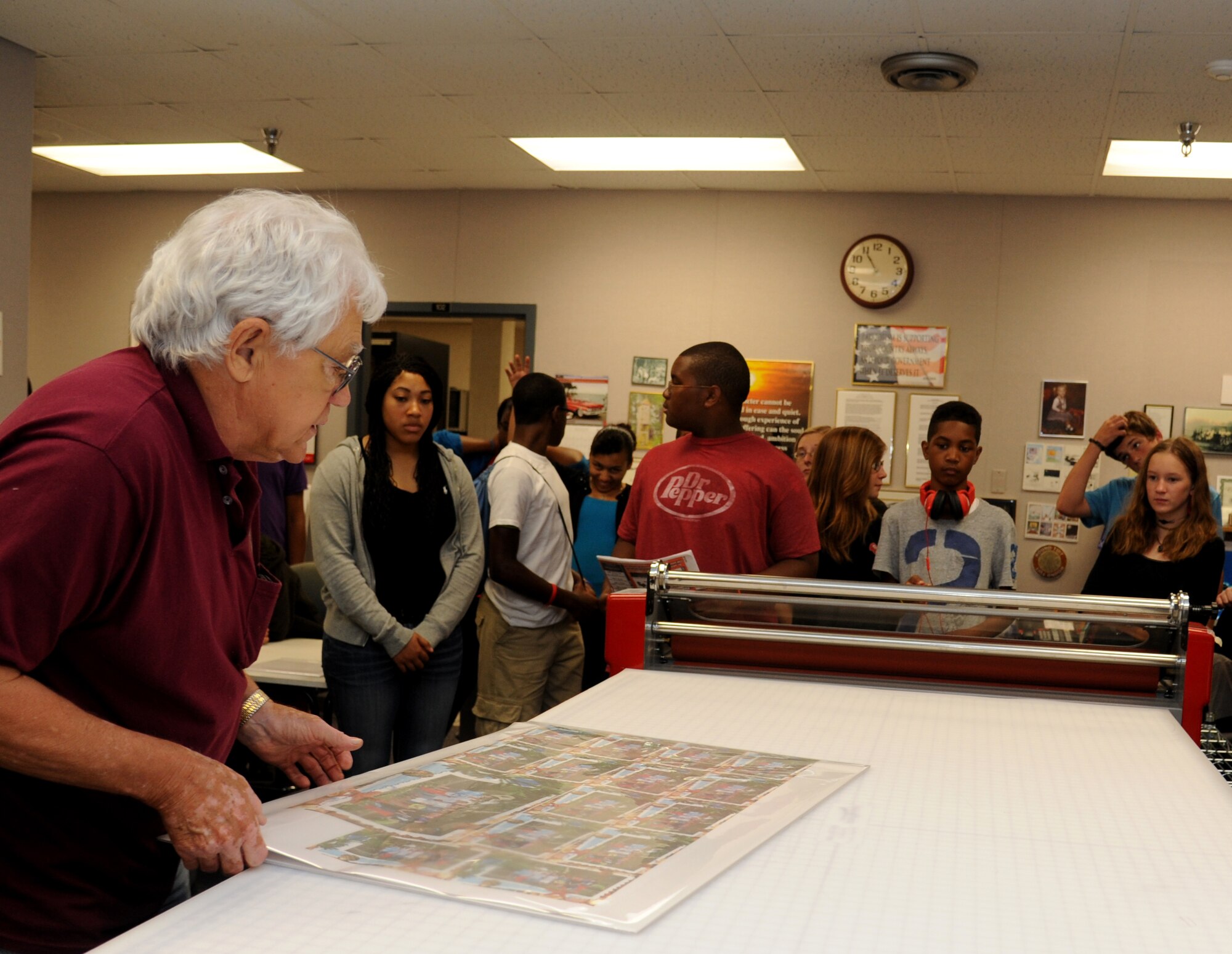 Terry Lee, K-Mar Industries contract illustrator, prepares a demonstration on how a poster is mounted and laminated to children from the youth center June 21, 2013, at Wall Studio, Keesler Air Force Base, Miss.  The youth center teen summer camp program also toured the public affairs office and other visual information services such as photo, video, graphics.  (U.S. Air Force photo by Kemberly Groue)