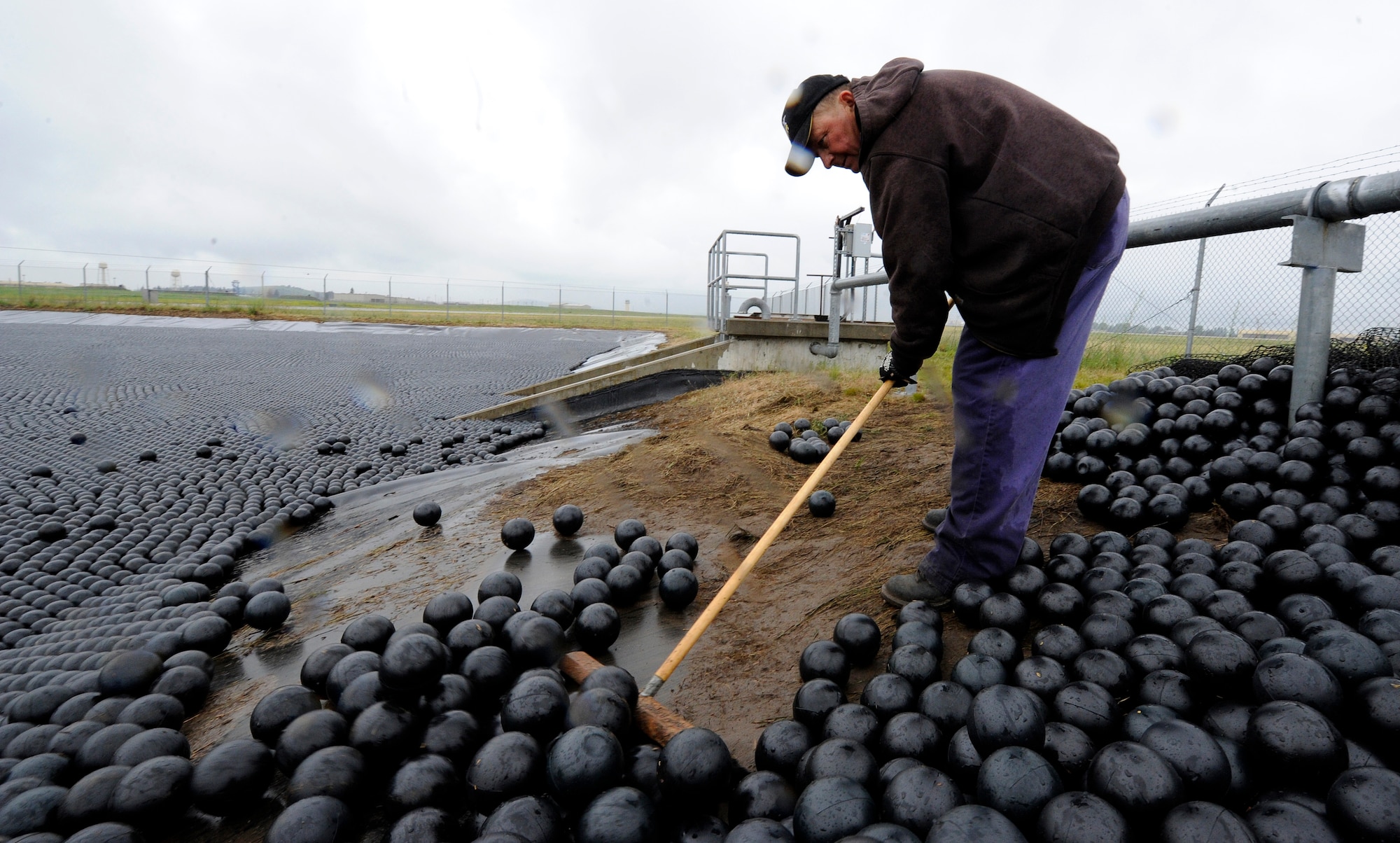 Greg Lucht, 92nd Civil Engineer Squadron equipment engineer operator, pushes bird balls into a natural pond located on the flight line at Fairchild Air Force Base, Wash., June 19 2013. The purpose of the bird balls is to allow access to the pond, while not attracting any wildlife to its location. (U.S. Air Force photo by Airman 1st Class Ryan Zeski/Released)