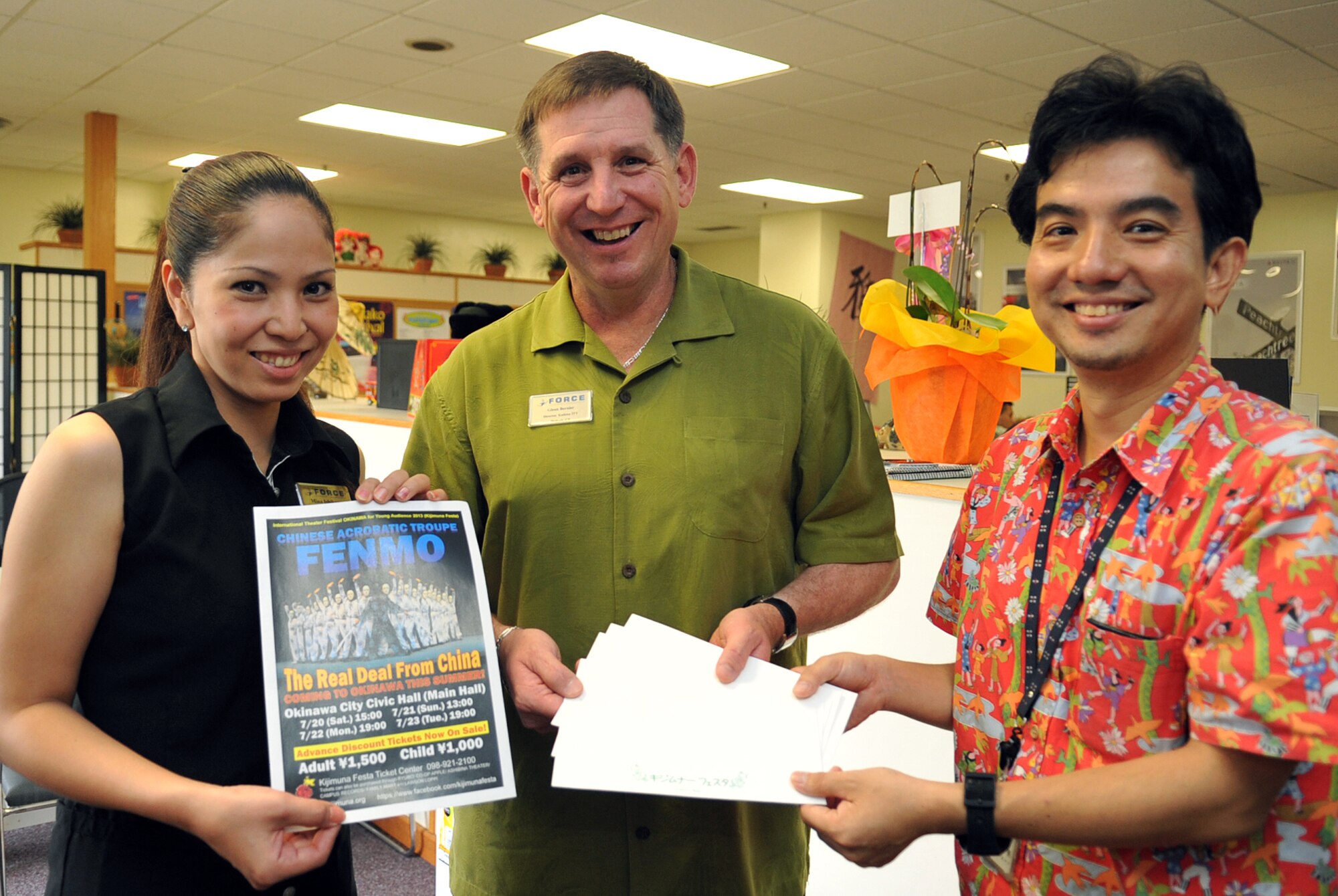 Ryo Tengan (right), Okinawa City Culture and Tourism Division chief, donates 10 tickets to Kijimuna Festa to Glenn Bernier (middle), 18th Forces Support Squadron Kadena Information Tickets & Travel director, and Minako Ishikawa (left), 18th FSS tour agent, at the Schilling Community Center on Kadena Air Base, Japan, June 26, 2013. This festival illustrates different performing arts and is hosted throughout Okinawa City. (U.S. Air Force photo by Naoto Anazawa/Released)