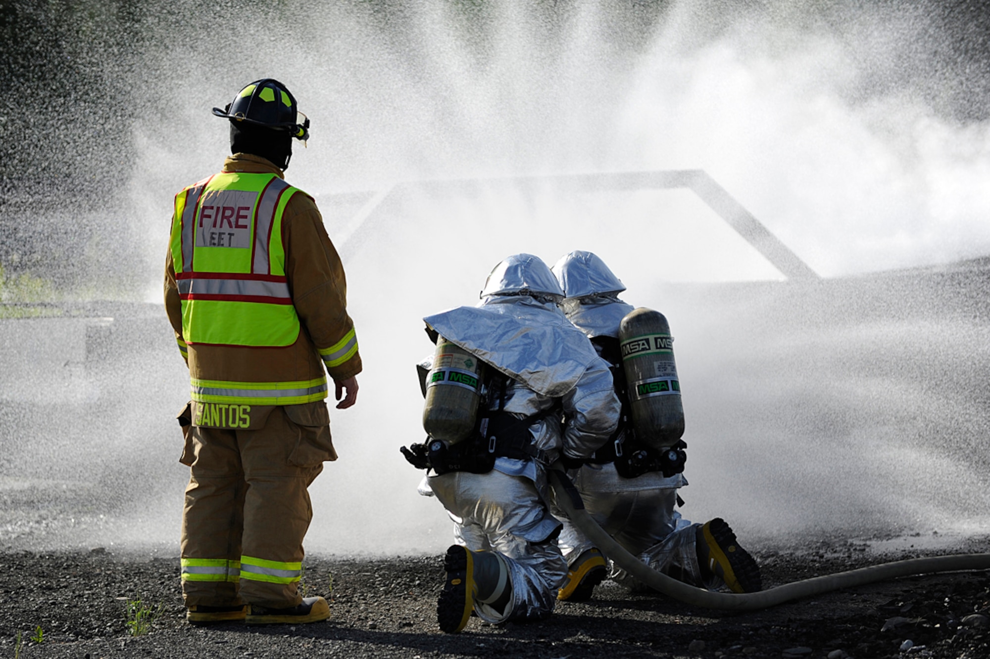 Air Force Master Sgt. Glen Santos II (left), 673d Civil Engineer Squadron exercise evaluation team member, watches as two Joint Base Elmendorf-Richardson firefighters extinguish a fire during an emergency management exercise, June 20, 2013. The exercise simulated a mass casualty mishap that provided training for first responders and JBER personnel. (U.S. Air Force photo/Staff Sgt. Zachary Wolf)