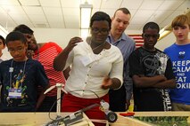 Destini Entzminger and Kevin Hovis (center), a technologist who works for Marine Corps Systems Command’s  Marine Air-Ground Task Force Command, Control and Communications Program Management Office, watch a LEGO robot cross a balsa wood bridge June 21 at Quantico Middle/High School. Destini was one of more than 40 students who attended the annual week-long Quantico Summer Academy, a Science, Technology, Engineering and Mathematics camp.