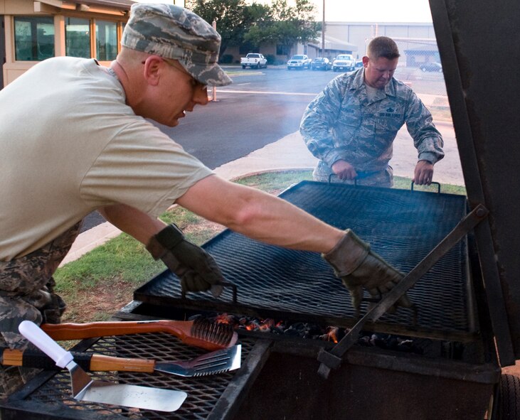 U.S. Air Force Master Sgt. Michael Moore, 7th Munitions Squadron first sergeant, left, and U.S. Air Force Master Sgt. Gerrick Hoffman, 7th Aircraft Maintenance Squadron first sergeant, place a rack on a grill June 26, 2013, at Dyess Air Force Base, Texas. The Dyess first sergeants hosted a burger burn to raise morale and interact with night shift workers. (U.S. Air Force photo by Airman 1st Class Peter Thompson/Released)