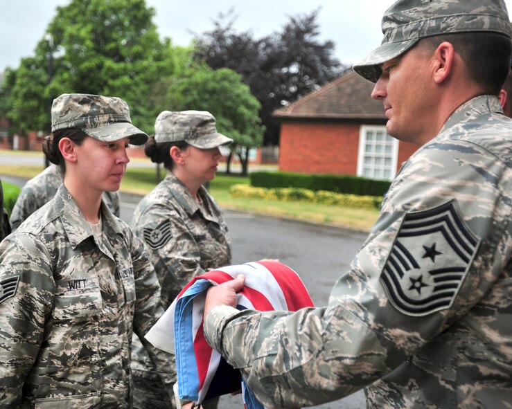 Chief Master Sgt. Tracy Jones, 100th Air Refueling Wing command chief, receives the Royal Air Force ensign from Staff Sgt. Amber Witt, 100th Operations Group, following the base retreat ceremony June 28, 2013, at RAF Mildenhall, England. A team of NCOs and Airmen secured both the U.S. flag and the RAF ensign as part of the ceremony that honors the colors and signals the official end of the duty day. (U.S. Air Force photo by Master Sgt. Brian M. Boisvert/Released)