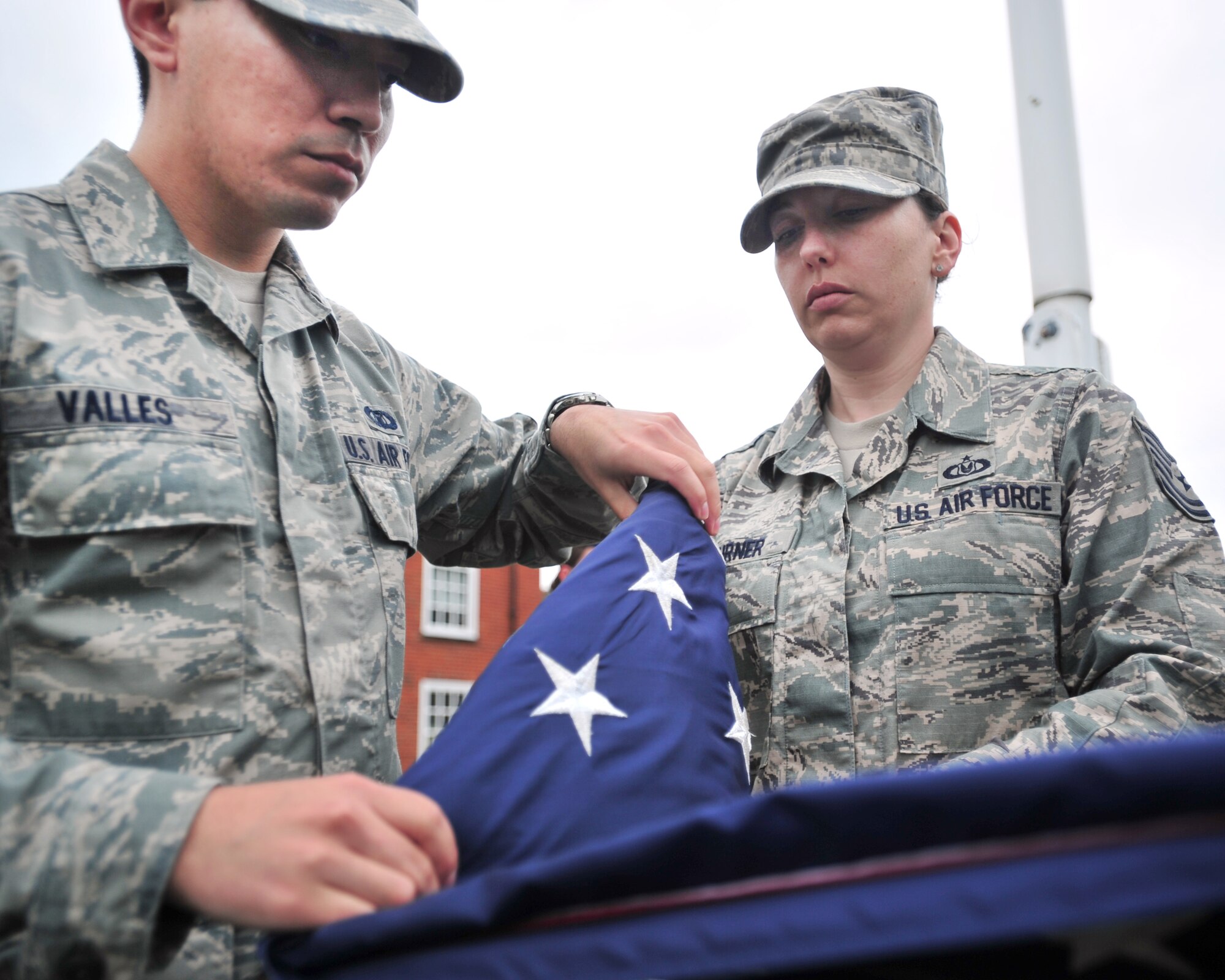 Tech. Sgt. Natalie Turner, Team Mildenhall flag detail team NCO in charge, helps Airman 1st Class Marcos Valles, 100th Operation Support Squadron Air Traffic Controller journeyman, fold the U.S. flag during the monthly retreat ceremony June 28, 2013, on RAF Mildenhall, England. A retreat ceremony, in which the U.S. flag and Royal Air Force ensign are retired, takes place on the last Friday of every month. (U.S. Air Force photo/Master Sgt. Brian M. Boisvert/Released)