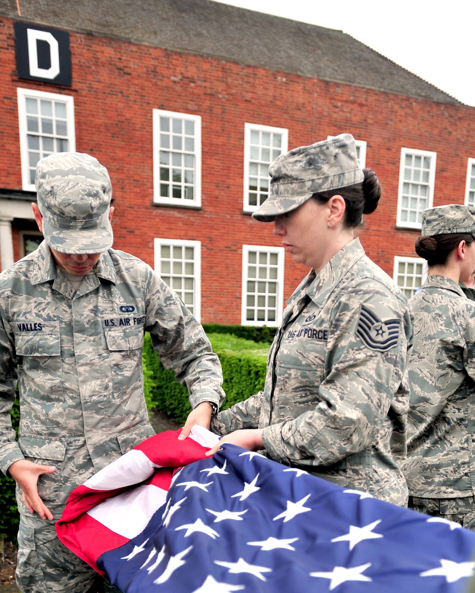 Tech. Sgt. Natalie Turner, Team Mildenhall flag detail team NCO in charge, helps Airman 1st Class Marcos Valles, 100th Operation Support Squadron Air Traffic Controller journeyman, fold the U.S. flag during the monthly retreat ceremony June 28, 2013, on RAF Mildenhall, England. A retreat ceremony, in which the U.S. flag and Royal Air Force ensign are retired, takes place on the last Friday of every month. (U.S. Air Force photo/Master Sgt. Brian M. Boisvert/Released)