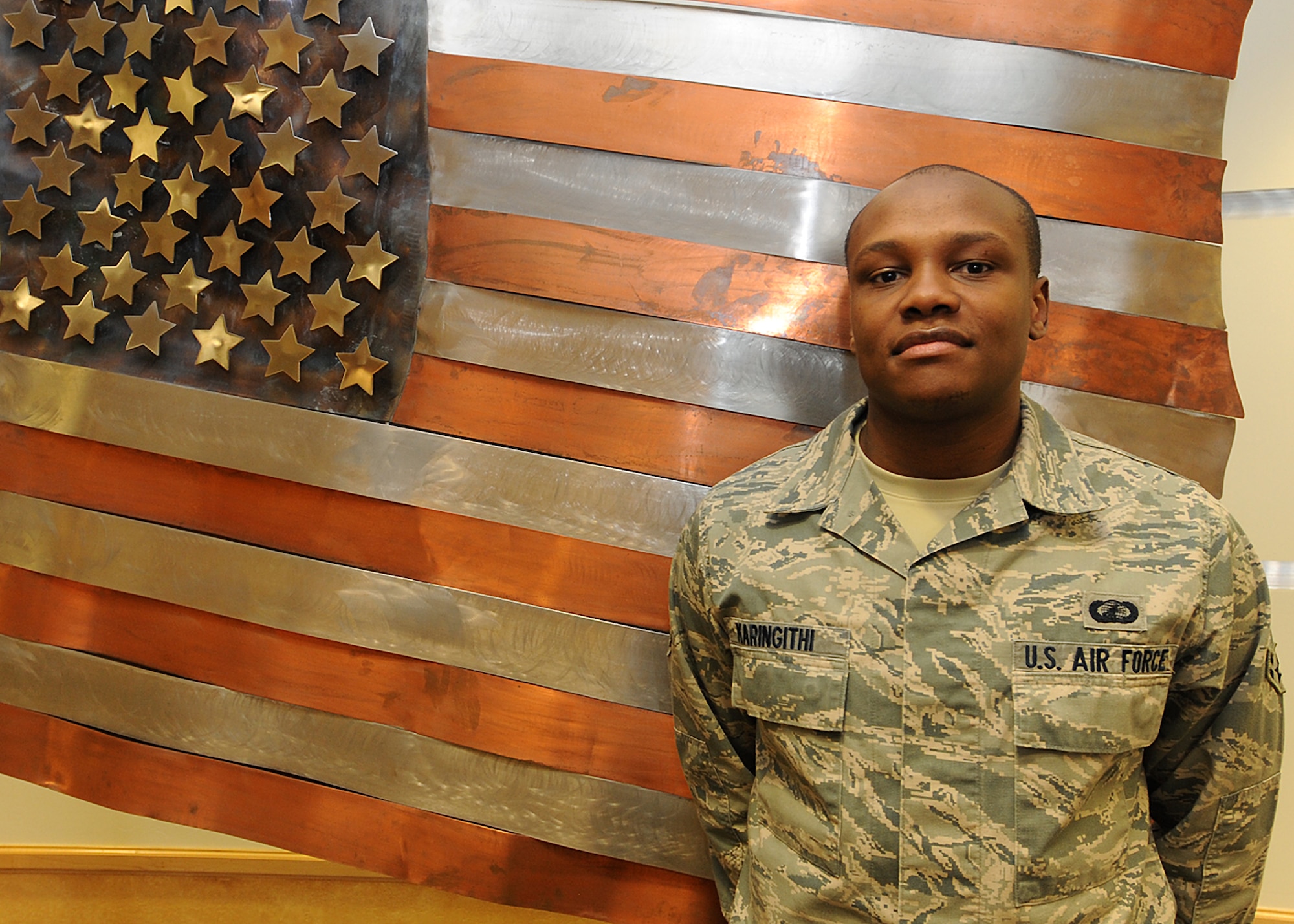 Airman 1st Class Jeff N. Karingithi , a contracting specialist from the 319th Contracting Flight, poses for a photo next to a metallic U.S. flag located inside Heritage Hall on Grand Forks Air Force Base, N.D. Karingithi became a United States citizen in a Fargo, N.D. federal courthouse, Jan. 11, 2013, at the age of 27. (U.S. Air Force photo/ Airman 1st Class Zachiah Roberson)