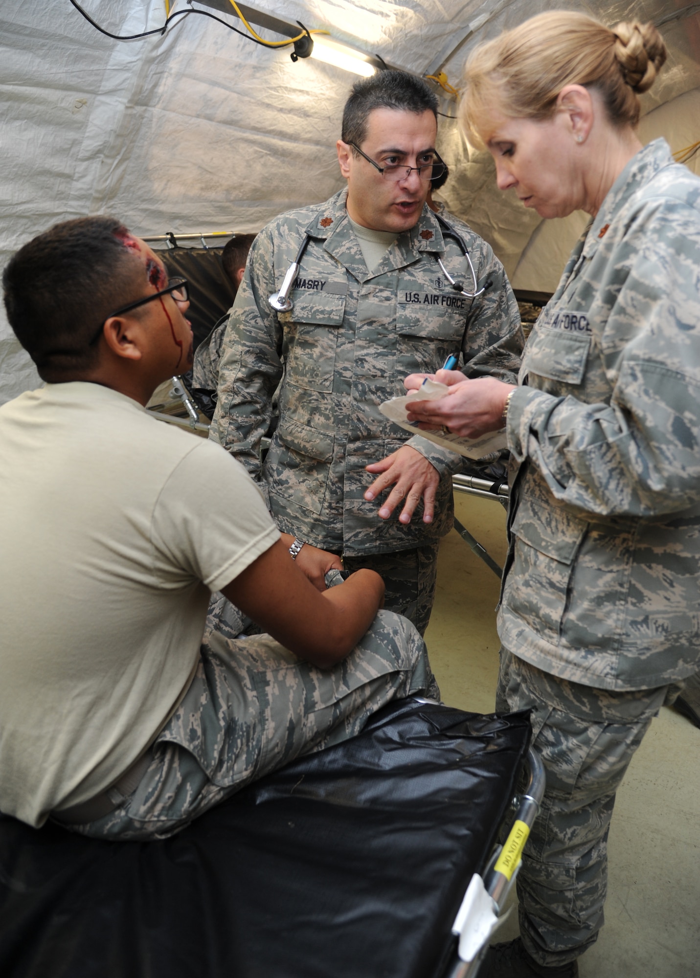Airman Basic Jose Brojas-Diaz, 336th Training Squadron, receives medical treatment from Majs. Salah Masry and Shelly Pardini, 81st Medical Operations Squadron, inside the temporary medical facility during a disease containment plan and point of dispensing exercise Feb. 28, 2013, near the Vandenburg Community Center, Keesler Air Force Base, Miss.  The scenario included a series of biological attacks in which numerous Keesler personnel became infected and the medical group had to distribute large quantities of medicine to efficiently minimize risk. (U.S. Air Force photo by Kemberly Groue)