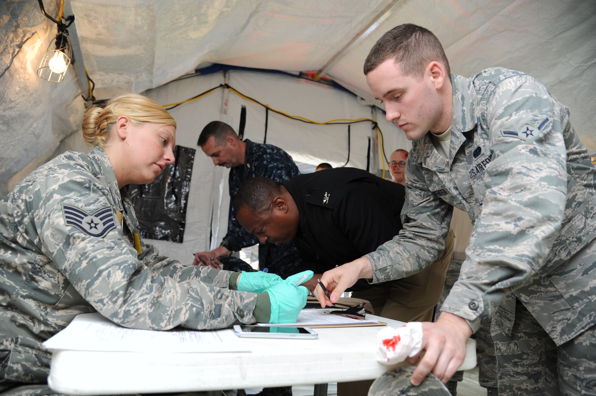 Staff Sgt. Kiley Pederson, 81st Medical Support Squadron, assists Airman Tyler Carpenter, 338th Training Squadron, at the patient administration table inside the temporary medical facility during a disease containment plan and point of dispensing exercise Feb. 28, 2013, near the Vandenburg Community Center, Keesler Air Force Base, Miss.  The scenario included a series of biological attacks in which numerous Keesler personnel became infected and the medical group had to distribute large quantities of medicine to efficiently minimize risk. (U.S. Air Force photo by Kemberly Groue)