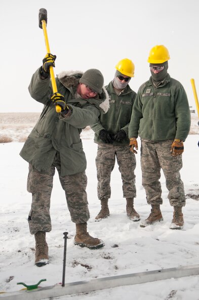 Senior Airman Cody Chappell, 90th Civil Engineer Squadron, drives a stake into the ground that holds down a piece of the frame for an Alaskan Small Shelter System while others wait for their turn at the hammer near Bldg 1331 Feb. 21. Junior members of the 90th CES set the tent up as part of a training exercise to gain familiarity with constructing the ASSS, which is a type of tent that can be outfitted with numerous environmental controls. (U.S. Air Force photo by Airman 1st Class Jason Wiese)