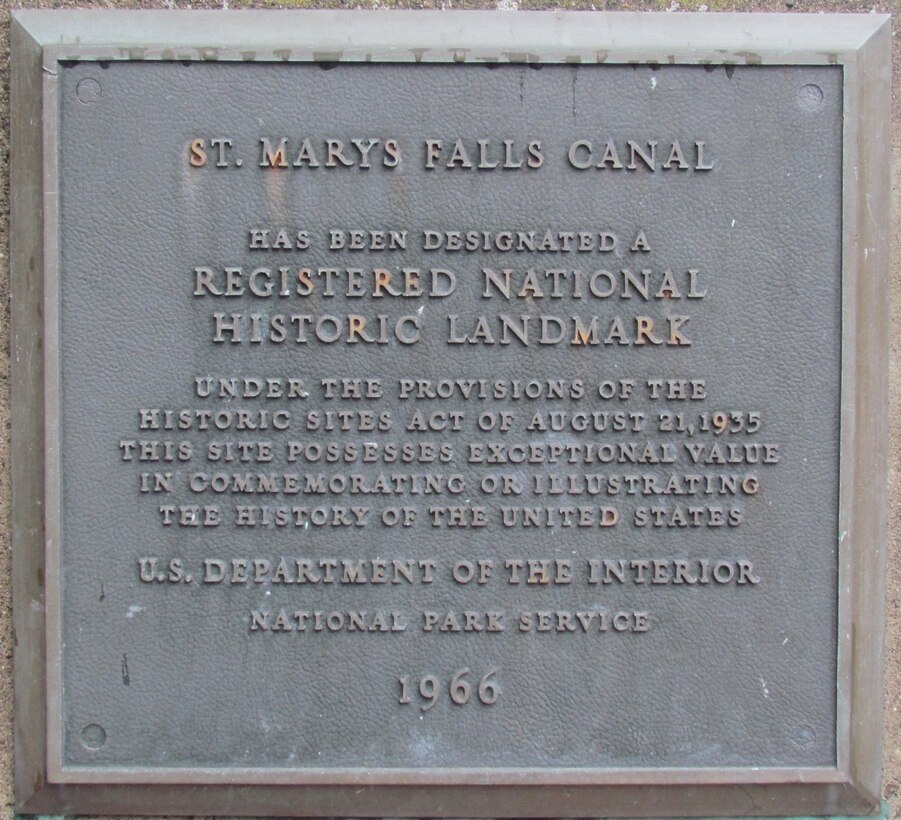 A brass plaque mounted near the main gates into the Upper Canal Park commemorates the designation of the Soo Locks as a National Historic Landmark.