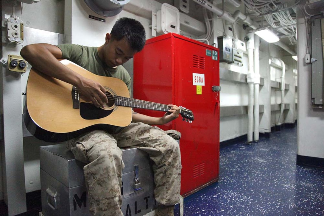 Corporal Bernard Vu, field radio operator, 2nd Platoon, Battery B, Battalion Landing Team 3/5, 15th Marine Expeditionary Unit, practices playing guitar aboard USS Rushmore, Feb. 27. While away, servicemembers find many ways to pass time while improving themselves and others physically, mentally and professionally.The 15th MEU is deployed as part of the Peleliu Amphibious Ready Group as a U.S. Central Command theater reserve force, providing support for maritime security operations and theater security cooperation efforts in the U.S. 5th Fleet area of responsibility. Vu, 20, is from Lincoln, Neb. (U.S. Marine Corps photo by Cpl. Timothy R. Childers/ Released)