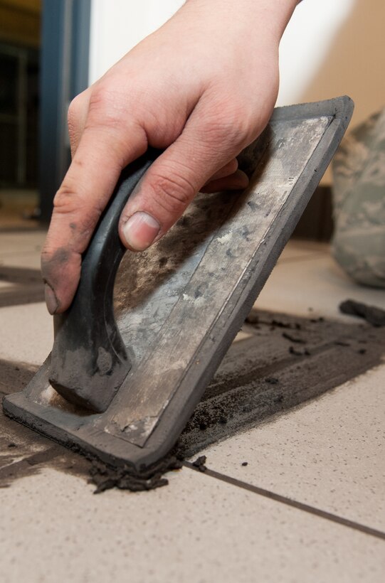 Senior Airman Omar Portillo, 28th Civil Engineer Squadron structural technician, applies grout to a bathroom tile floor in the 28th CES operations building on Ellsworth Air Force Base, S.D., Feb. 21, 2013. The grout must dry for 24 hours before the tile is cured to guarantee the floor is a flat, clean surface that will last years longer than the previous vinyl flooring. (U.S. Air Force photo by Airman 1st Class Kate Thornton-Maurer/Released)