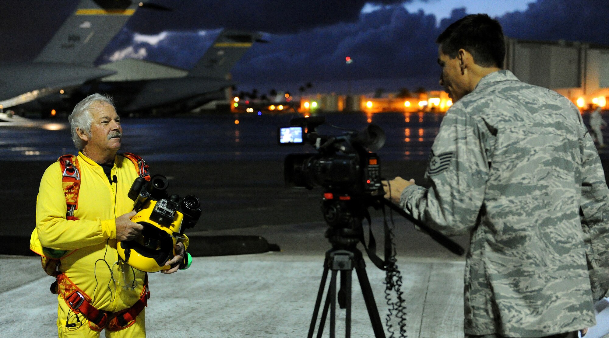 Tech. Sgt. Anthony Gomez, 15th Wing Public Affairs broadcaster (right) interviews Tom Sanders, freefall cameraman and skydiver cinematographer (left), prior to him boarding a C-17 Globemaster III at Joint Base Pearl Harbor Hickam-Hawaii, Feb. 26, 2013.  Sanders was on base to film a scene for an upcoming episode of “Hawaii Five-0” in which two Special Operations Command, Pacific jumpers perform a freefall jump as stunt doubles for the show’s actors.  During the interview, Sanders explained how he uses multiple video cameras attached to the top of his helmet to capture various video view point perspectives during his jumps. (U.S. Air Force photo/Tech. Sgt. Jerome S. Tayborn)