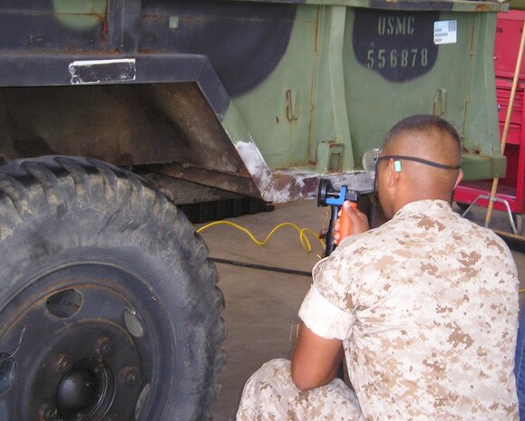 A Marine lance corporal in Okinawa, Japan, performs organizational-level surface preparation using the Corrosion Prevention and Control tool kit to remove corrosion prior to the application of touch-up paint on a trailer. The corrosion program, managed by Marine Corps Systems Command, has improved the readiness of USMC equipment and significantly reduced the cost of corrosion.