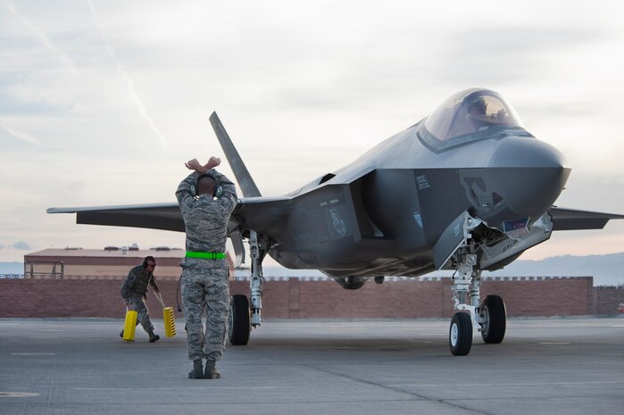 A U.S. Air Force crew chief assigned to the 57th Aircraft Maintenance Squadron Lightning Aircraft Maintenance Unit marshals an F-35 Lightning II aircraft into its parking spot after it's arrival at Nellis Air Force Base, Nev., March 6, 2013.  The two F-35s will be assigned to the 422nd Test and Evaluation Squadron. (U.S. Air Force photo by Lawrence Crespo)