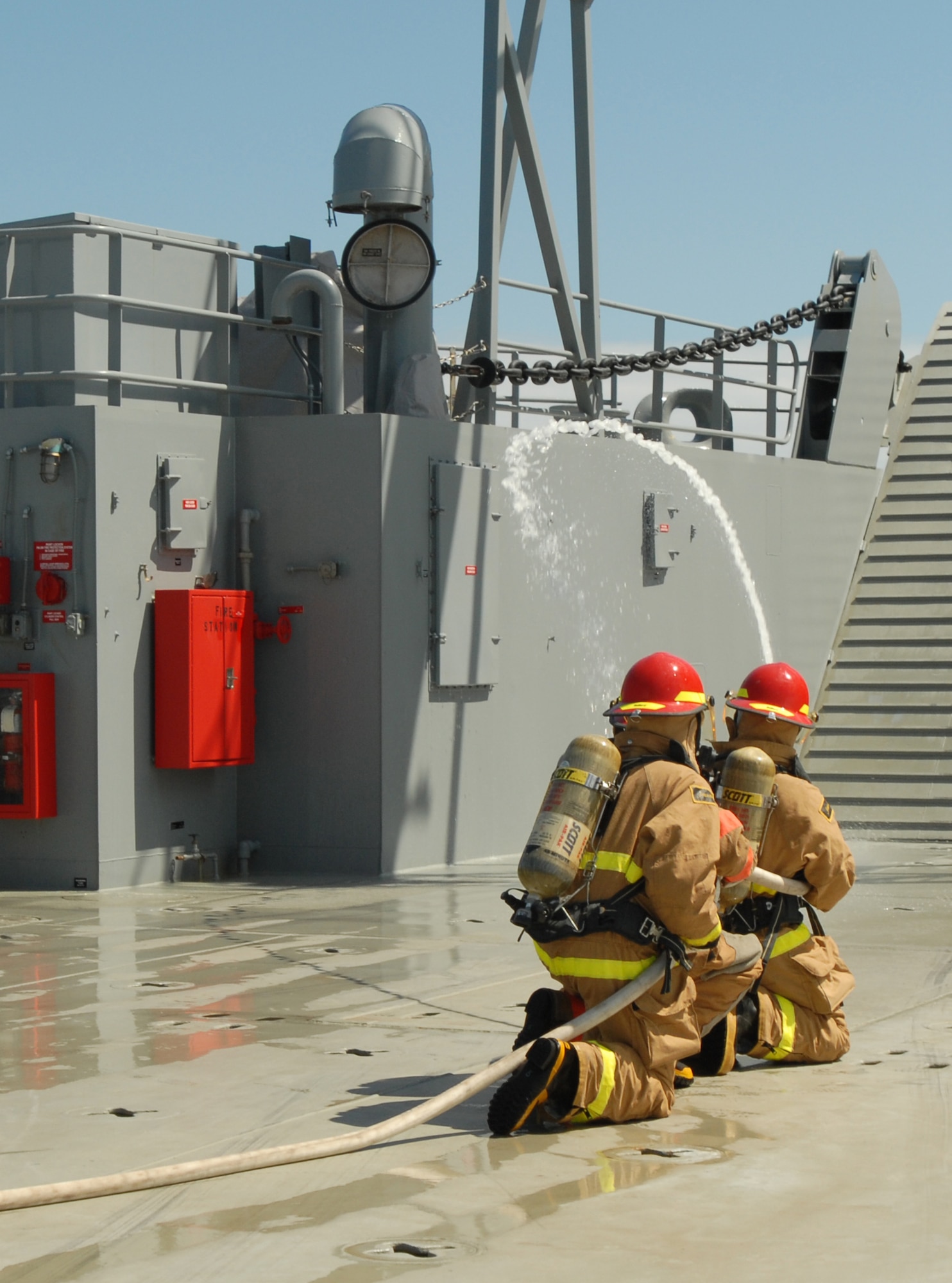 Crew members spray down the room where a simulated fire broke out onboard the LCU 2001 "Runnymede." If a fire were to break out, half of the fire team would immediately start spraying down the area of fire while the other half dons fireproof suits. Once half the team is dressed, they switch off positions so they can get dressed while still maintaining constant control of the fire. The crew is expected to take no more than two minutes to be fully dressed in fire protection gear. (U.S. Army photo by Sgt. Barbara J. Liau, 123rd Mobile Public Affairs Detachment)