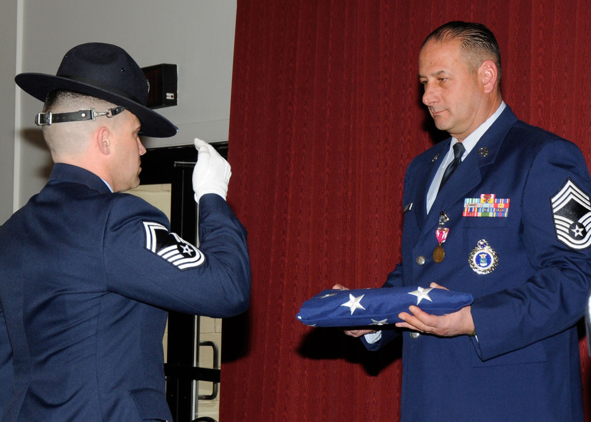 HANSCOM AIR FORCE BASE, Mass. -- Senior Master Sgt. Christopher McCool salutes the flag after presenting it to Chief Master Sgt. Alfred Wilkes during his retirement ceremony at the Minuteman Commons March 1. Wilkes, 319th Recruiting Squadron superintendent, retired after serving 30 years. (U.S. Air Force photo by Linda LaBonte Britt)