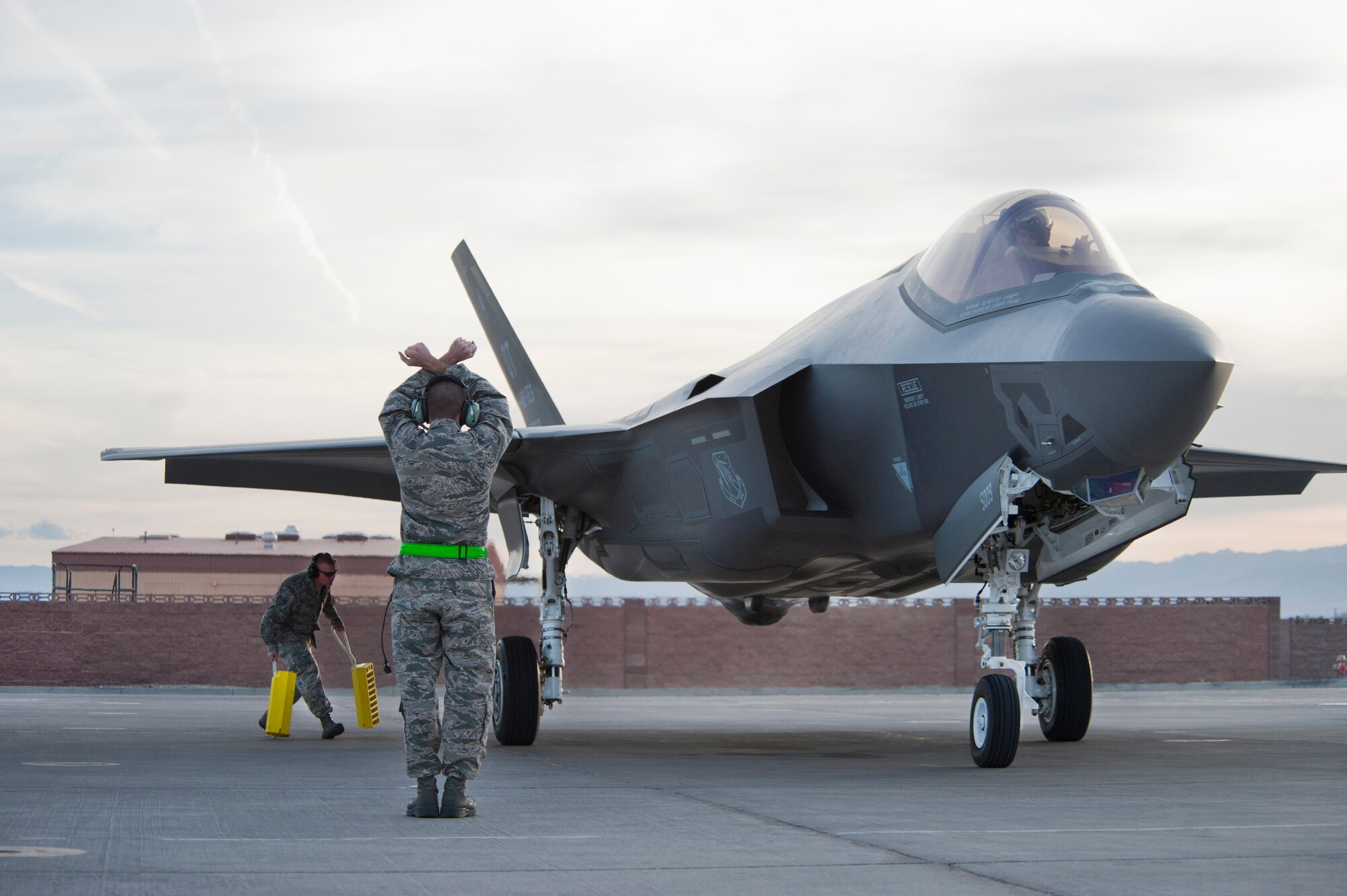 A crew chief assigned to the 57th Aircraft Maintenance Squadron Lightning Aircraft Maintenance Unit marshals an F-35 Lightning II into its parking spot after arriving Wednesday, March 6, 2013, at Nellis Air Force Base, Nev. The two F-35s will be assigned to the 422nd Test and Evaluation Squadron. (U.S. Air Force photo/Lawrence Crespo)