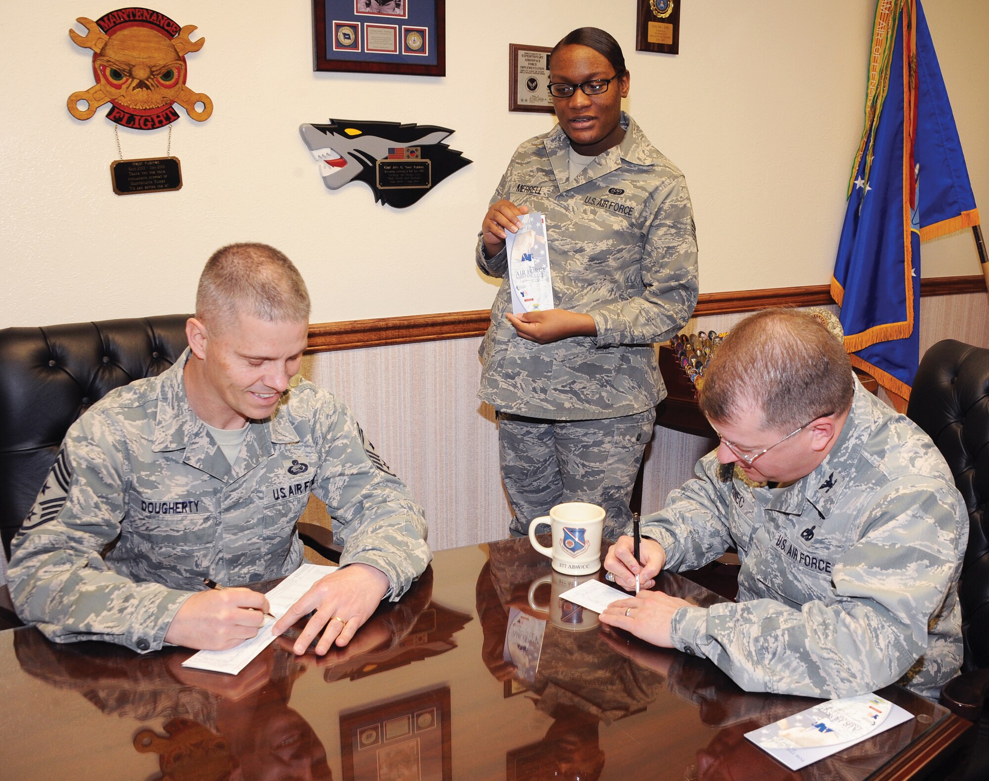 Chief Master Sgt. John Dougherty, command chief for the Air Force Nuclear Weapons Center and 377th Air Base Wing, left, and Col. John Kubinec, 377 ABW commander, right, sign their Air Force Assistance Fund pledge forms March 1 at Kirtland AFB. Staff Sgt. Kimberly Merrell, center, is an AFAF campaign keyworker for the 377 ABW staff.  